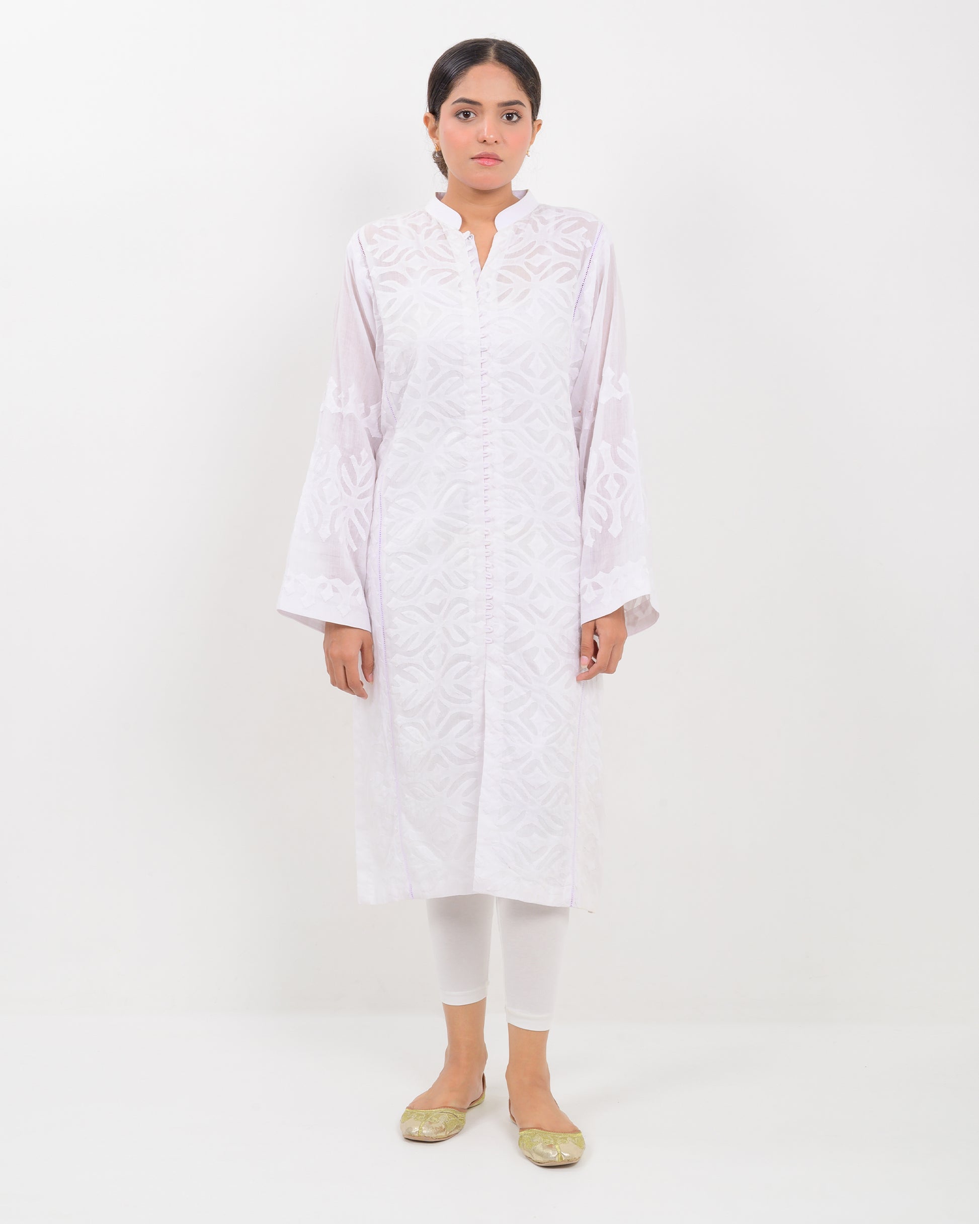 A woman wearing a handcrafted applique white shirt showcasing a subtle pattern.