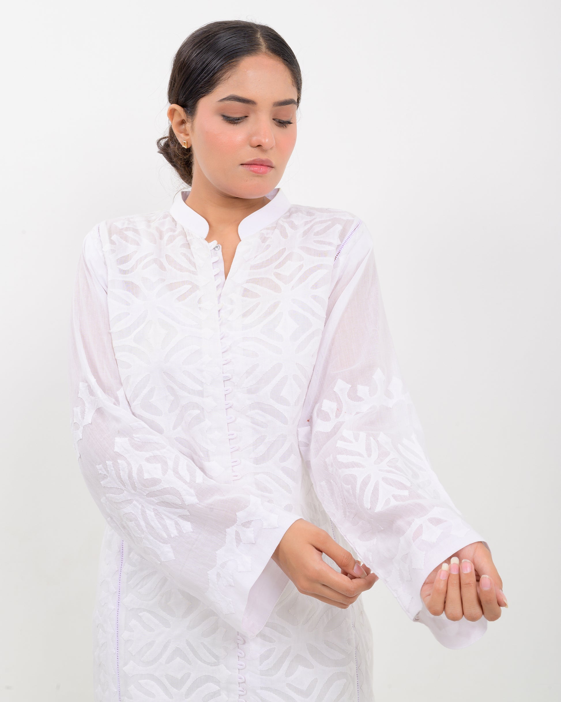 A woman wearing a handcrafted applique white shirt showcasing a subtle pattern against a white background