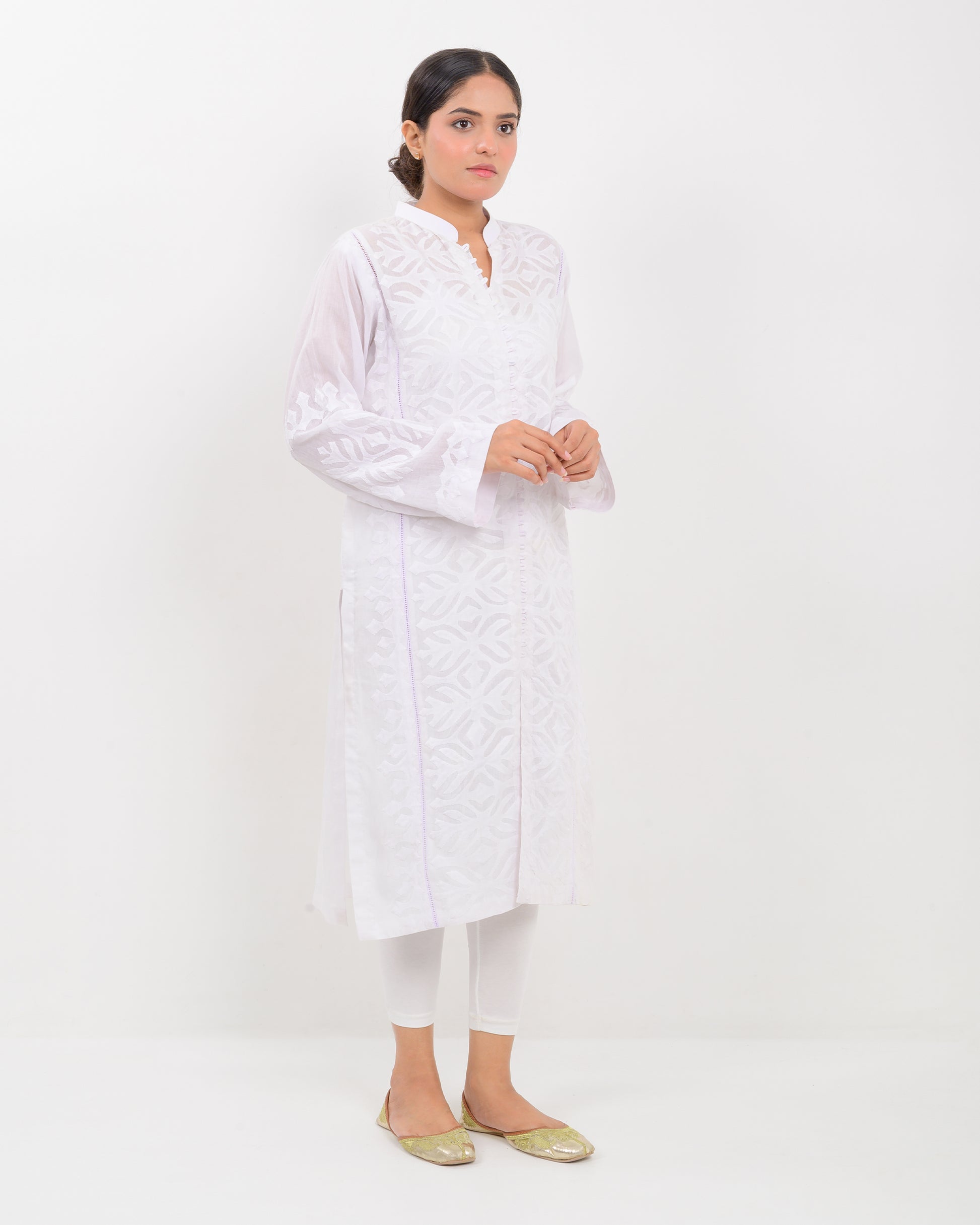 A woman wearing a handcrafted applique white shirt showcasing a subtle pattern against a white background