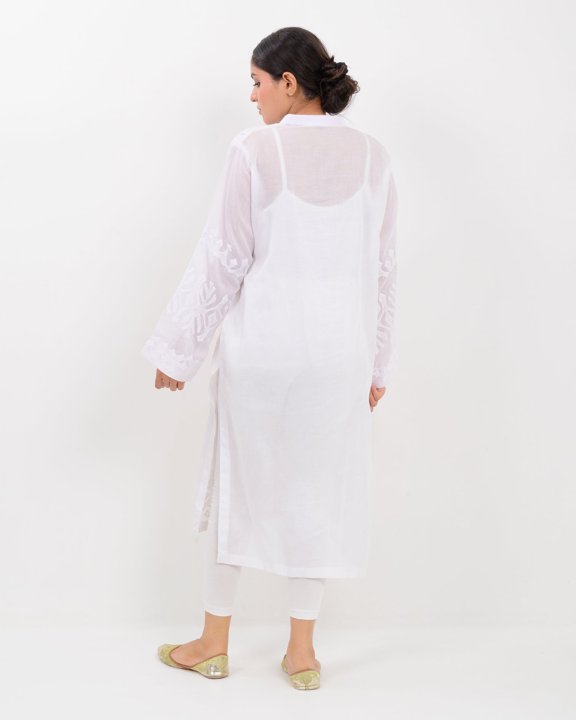 A woman wearing a handcrafted applique white shirt showcasing a subtle pattern against a white background