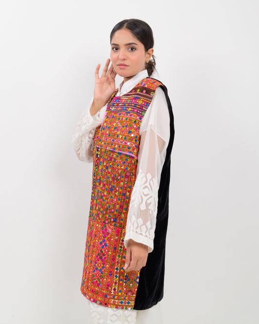 Woman wearing a colorful, patterned Balochi embroidery vest over a white shirt on a white background
