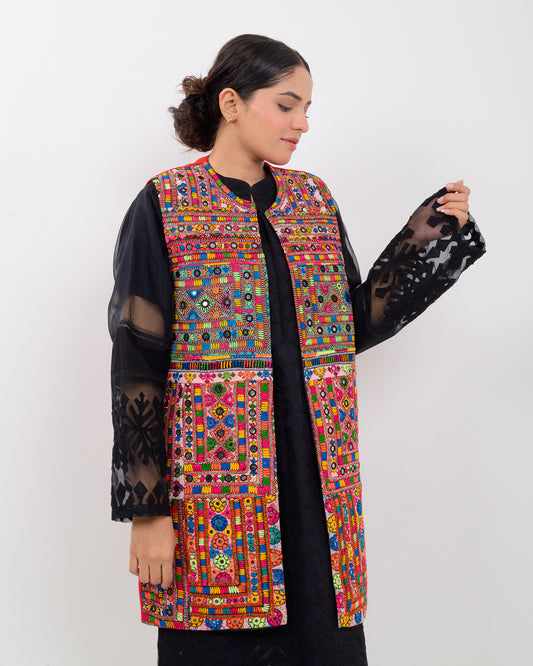 A woman wearing a colorful, patterned Balochi embroidery vest over a black outfit on a white background