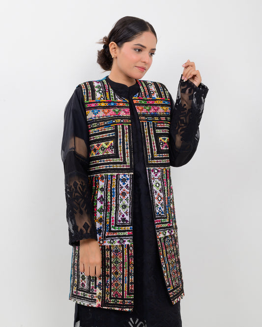 Woman wearing a colorful balochi embroidered vest over a black outfit on a white background