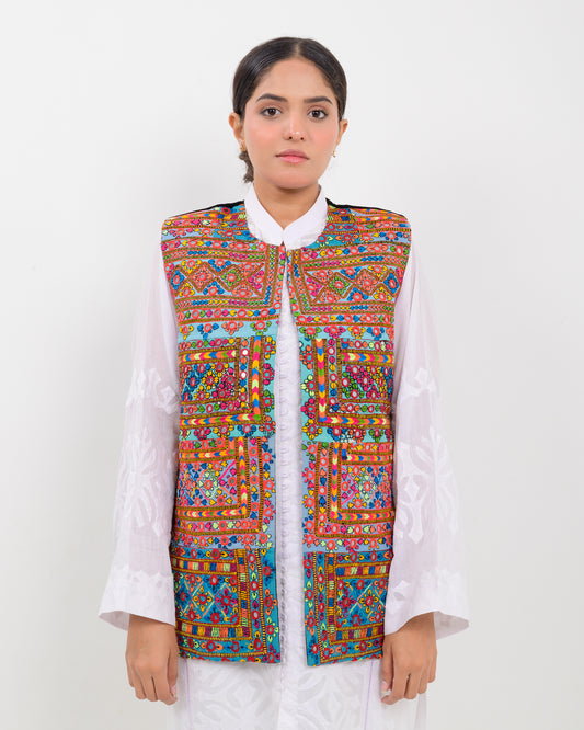 Woman wearing a colorful patterned Balochi embroidery vest over a white shirt on a white background