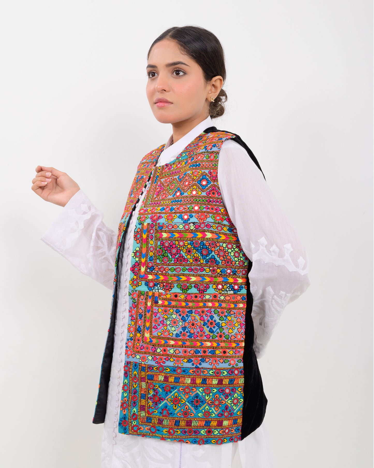 Woman wearing a colorful patterned Balochi embroidery vest over a white shirt on a white background