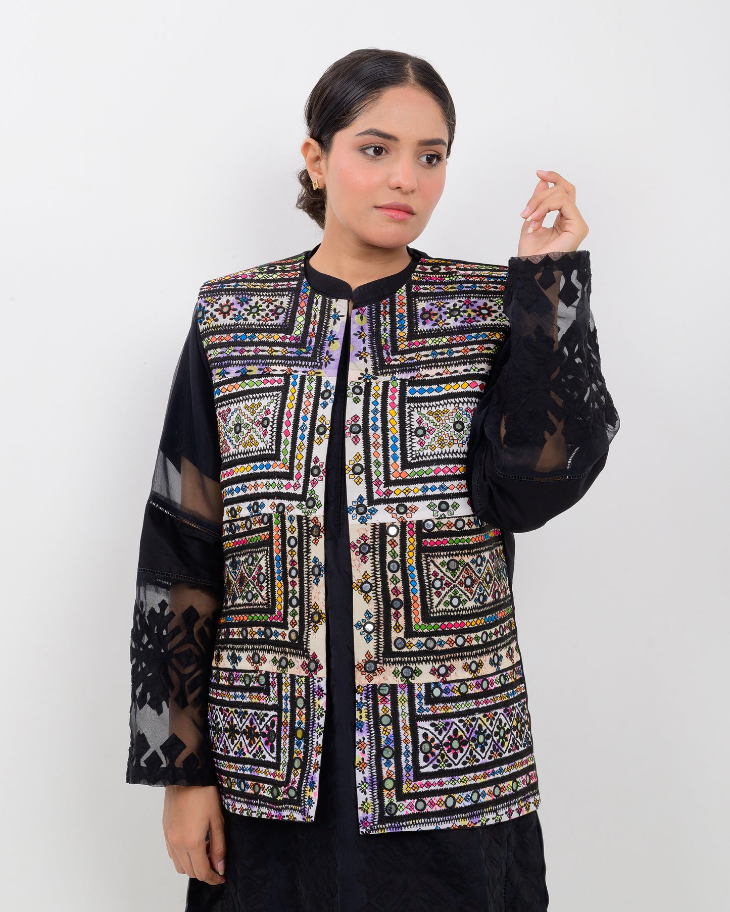 A woman wearing a colorful Balochi embroidered vest with sheer sleeves on a white background