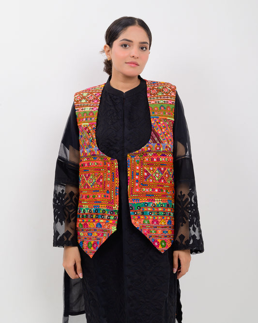 Woman wearing a colorful embroidered vest over a black outfit on a white background