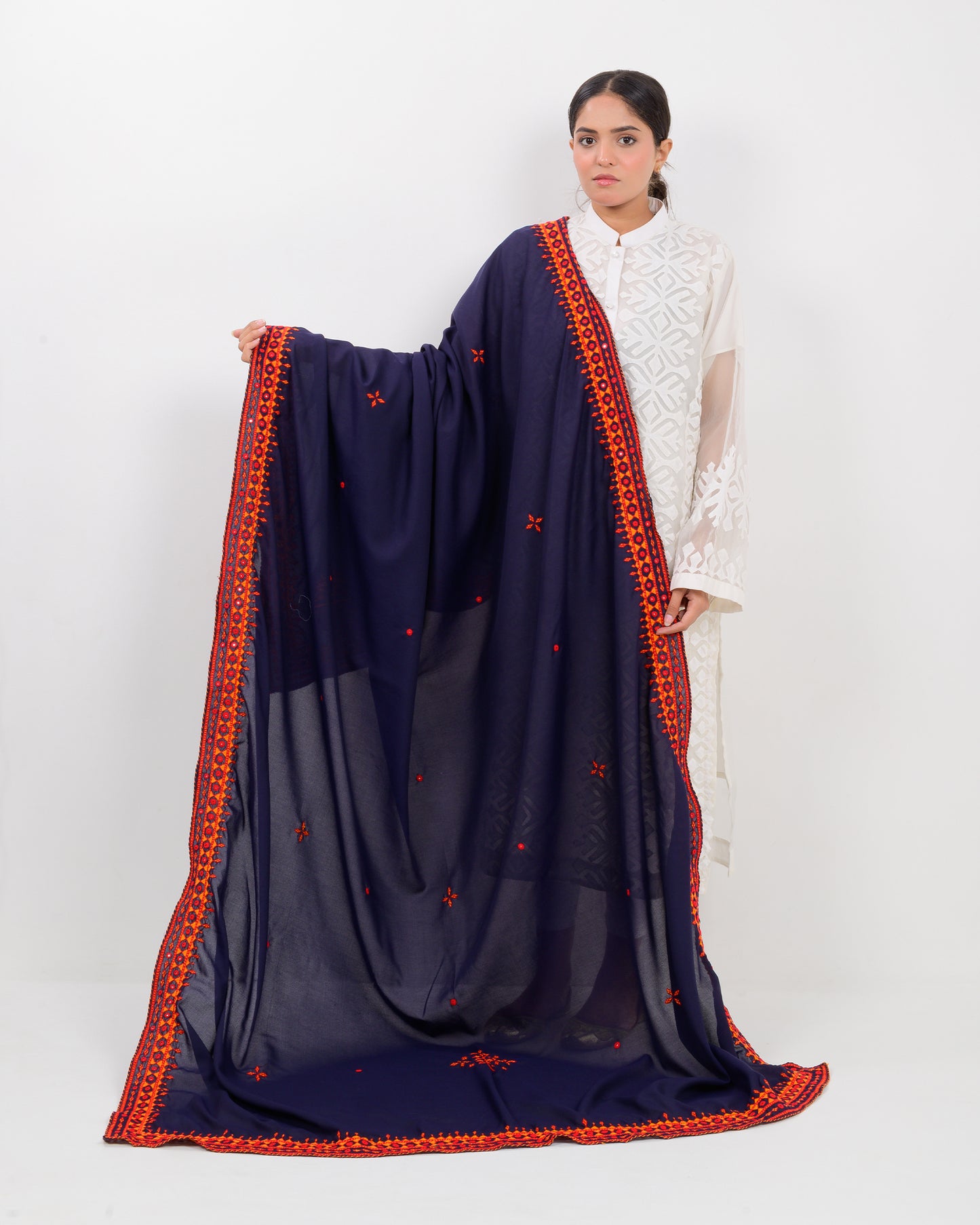 Woman wearing a navy blue shawl with orange embroidery on a white background