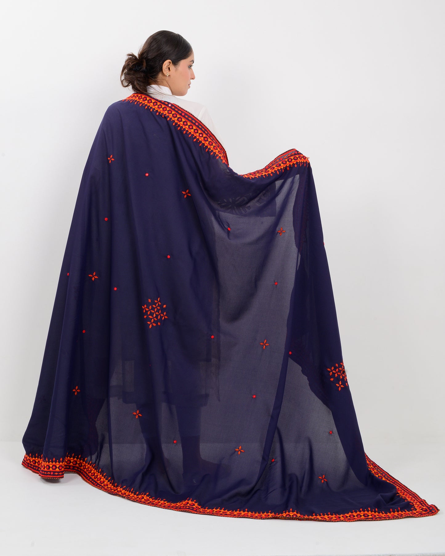 Woman wearing a navy blue shawl with orange embroidery on a white background