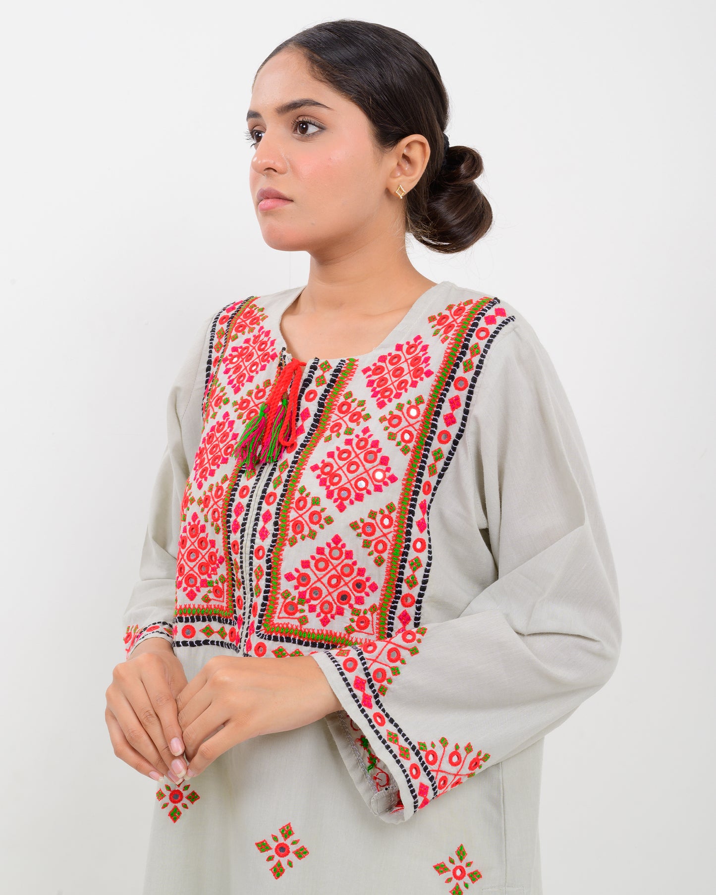 A woman wearing a light gray Balochi embroidery shirt on a white background