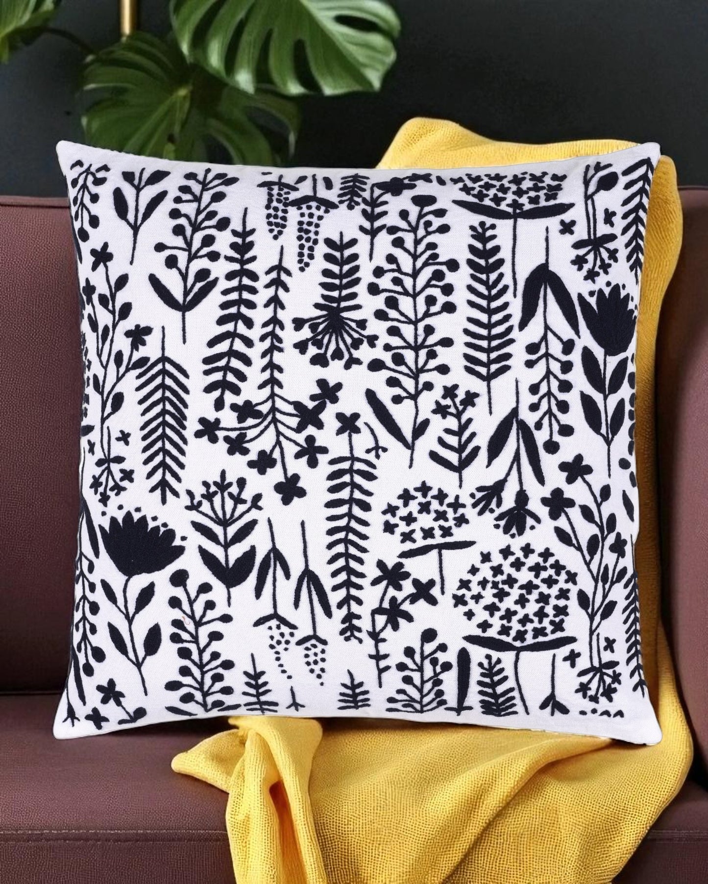 Decorative pillow with black floral pattern on white background, placed on a couch with yellow blanket.