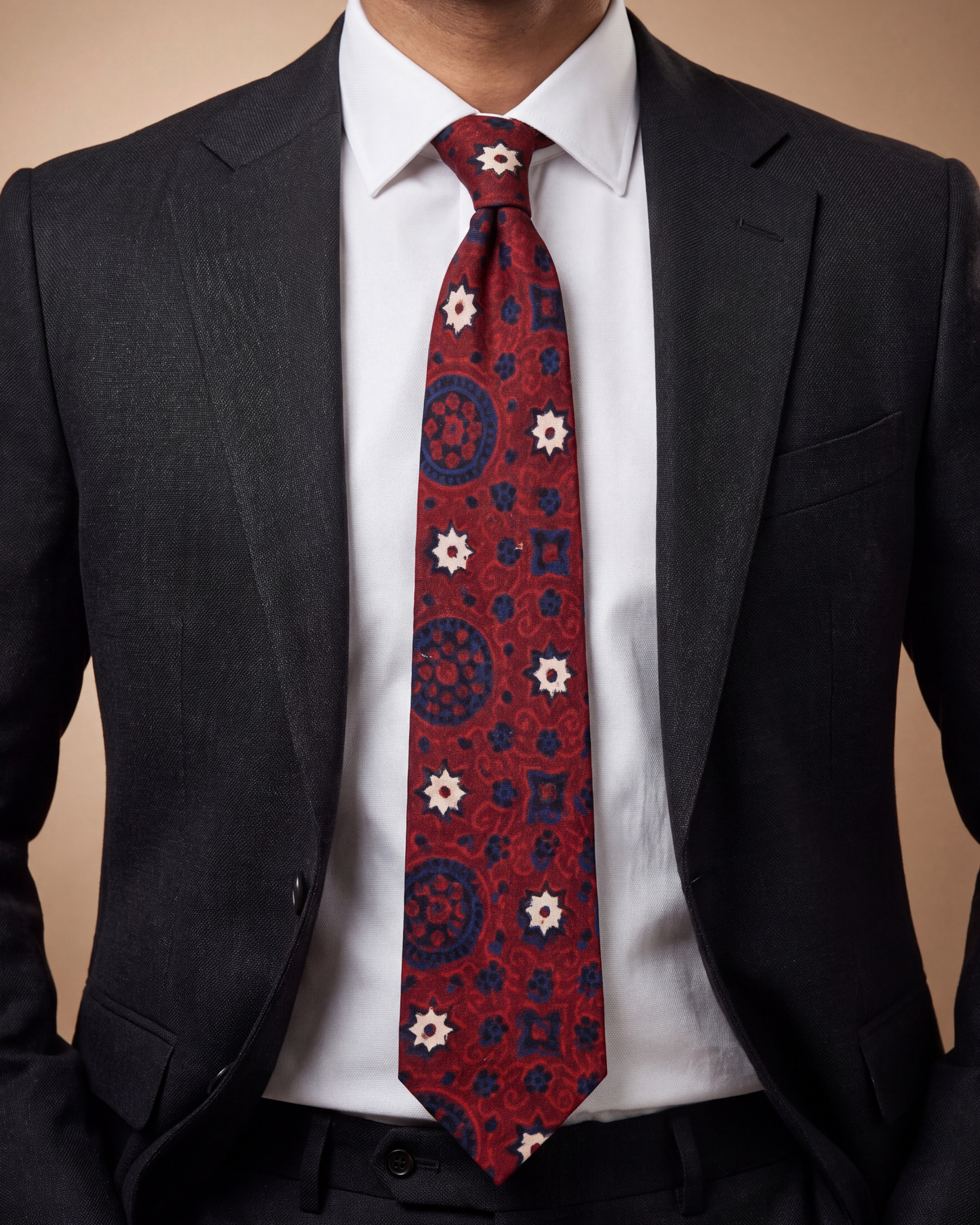 A men's necktie with a red base and a blue and white geometric pattern, styled on a model wearing a white dress shirt and a dark gray suit jacket.