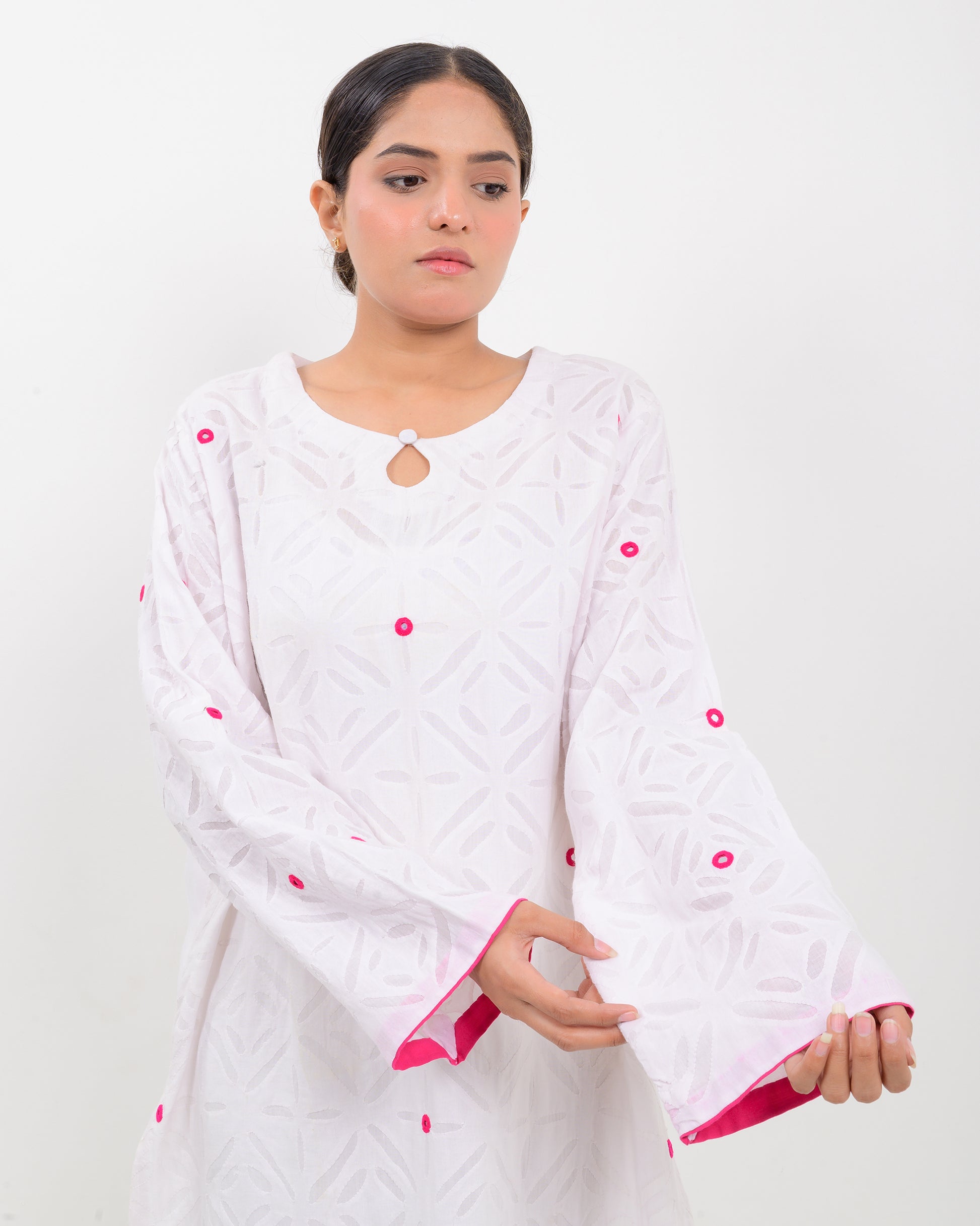 A woman wearing a white shirt with pink embroidery on a white background