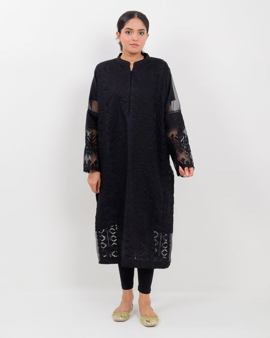 Woman wearing a black hand-crafted applique cutwork shirt with sheer sleeves against a white background