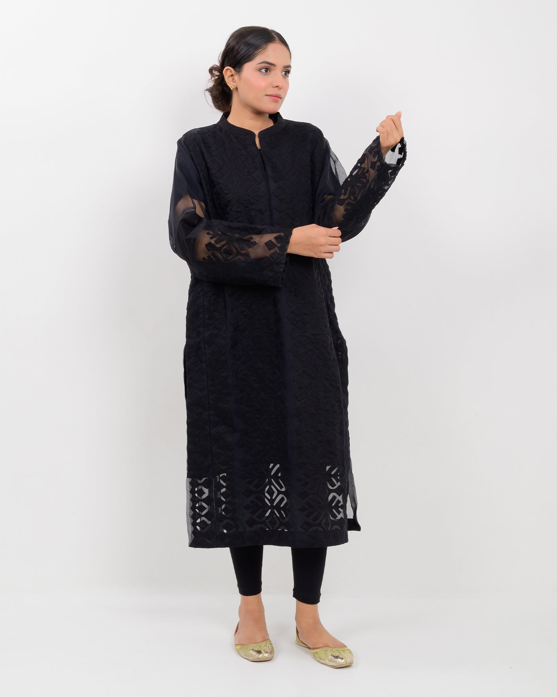 Woman wearing a black hand-crafted applique cutwork shirt with sheer sleeves against a white background