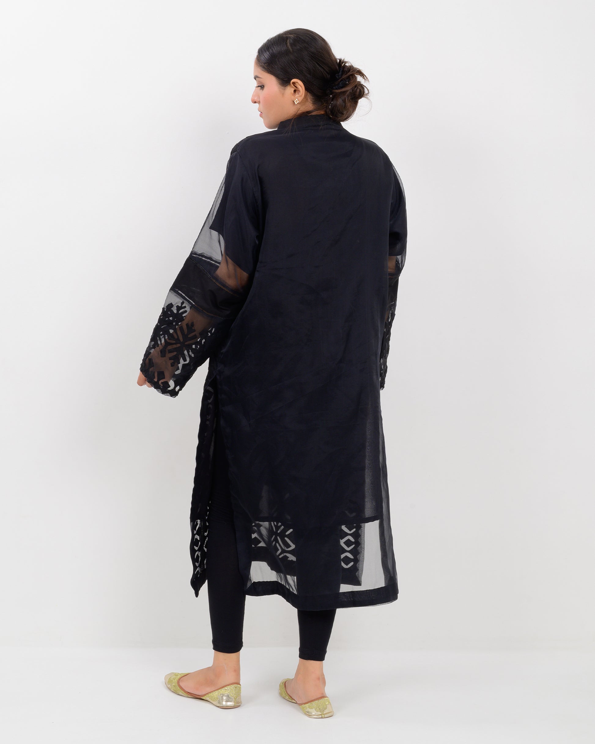Woman wearing a black hand-crafted applique cutwork shirt with sheer sleeves against a white background