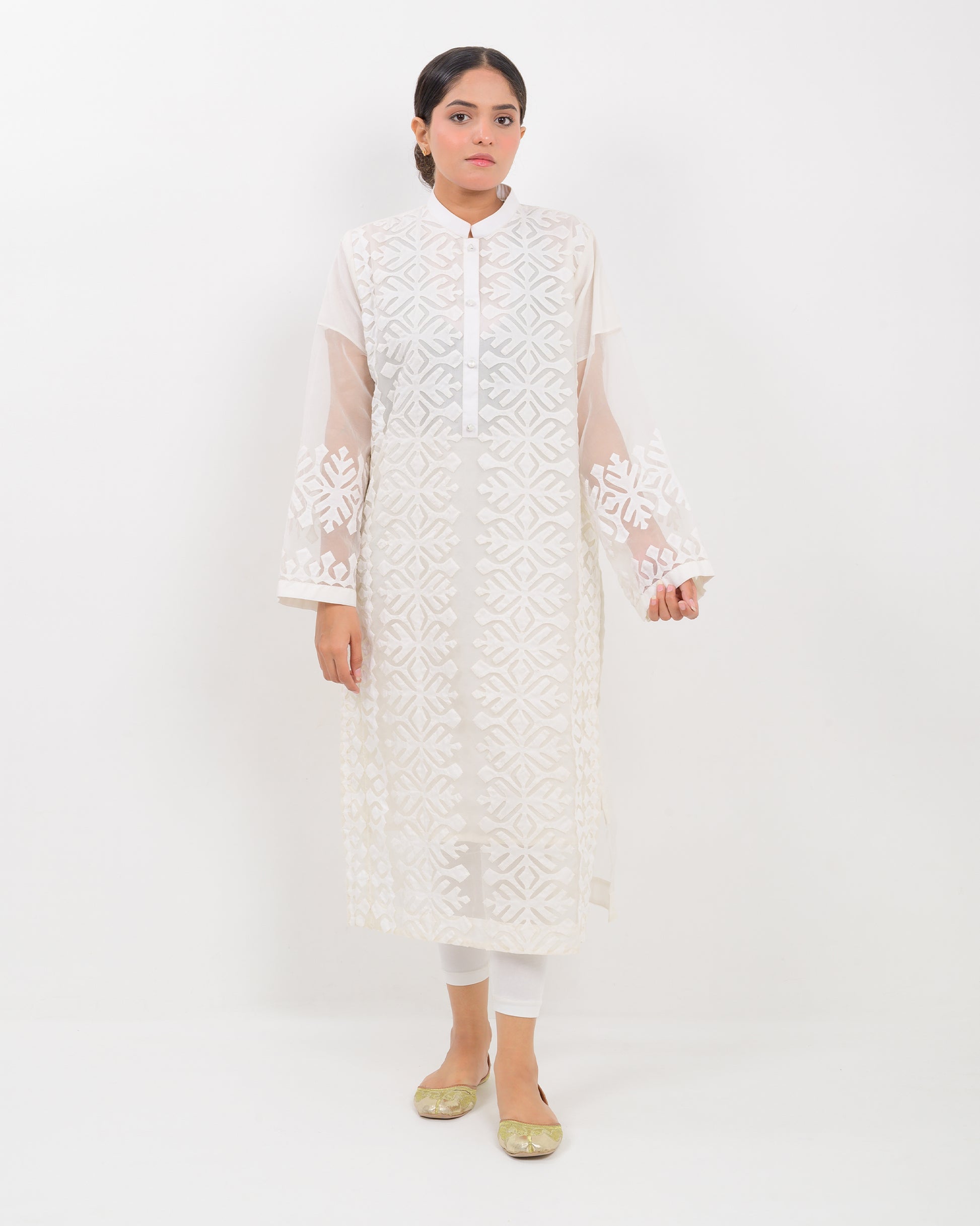 Woman wearing a white hand-crafted applique cutwork shirt with sheer sleeves against a white background