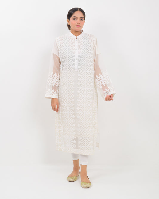 Woman wearing a white hand-crafted applique cutwork shirt with sheer sleeves against a white background