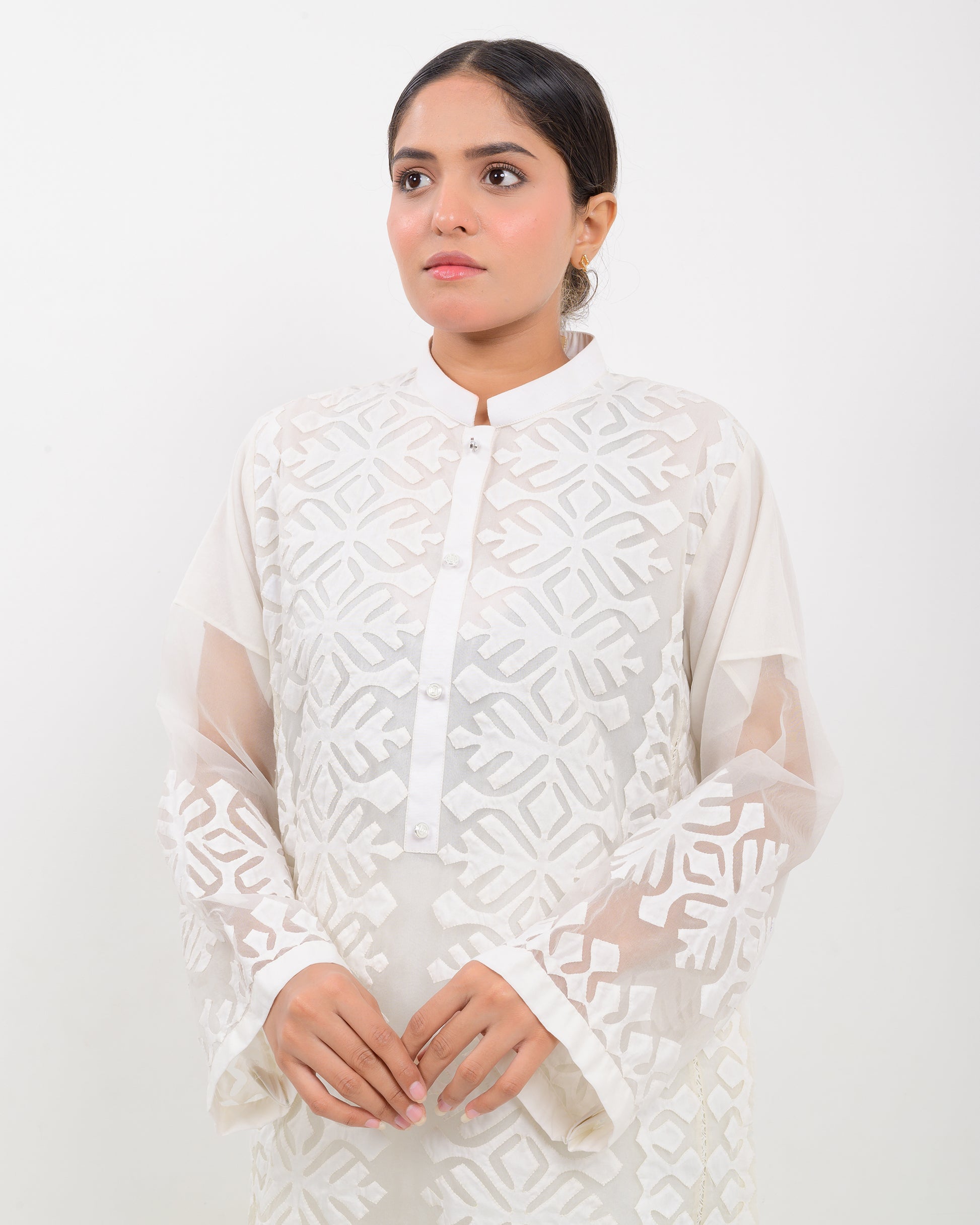 Woman wearing a white hand-crafted applique cutwork shirt with sheer sleeves against a white background