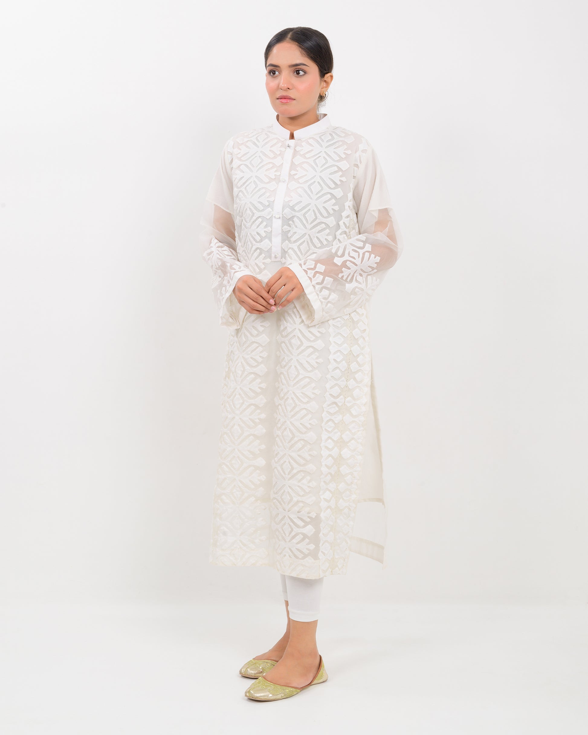 Woman wearing a white hand-crafted applique cutwork shirt with sheer sleeves against a white background