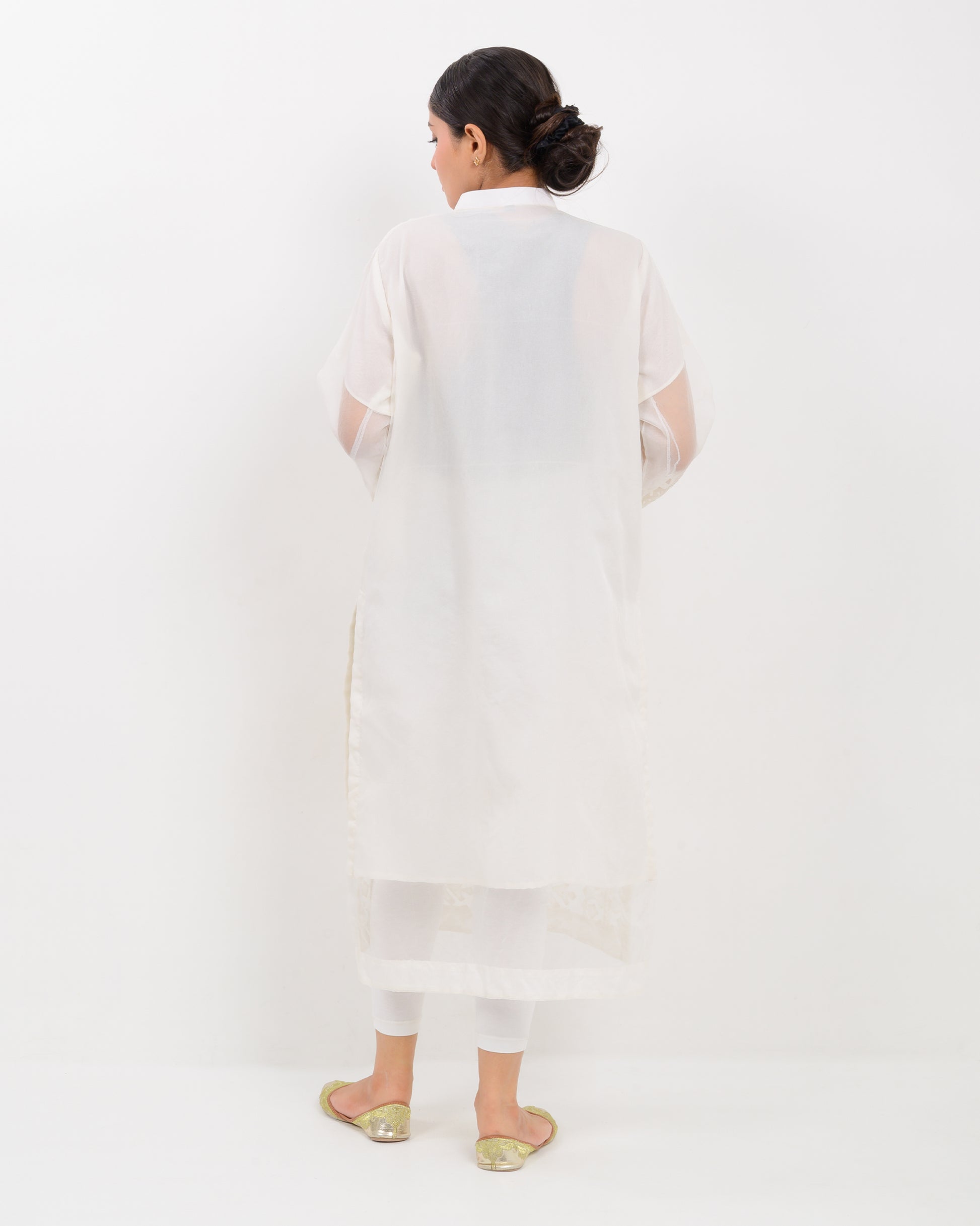 Woman wearing a white hand-crafted applique cutwork shirt with sheer sleeves against a white background