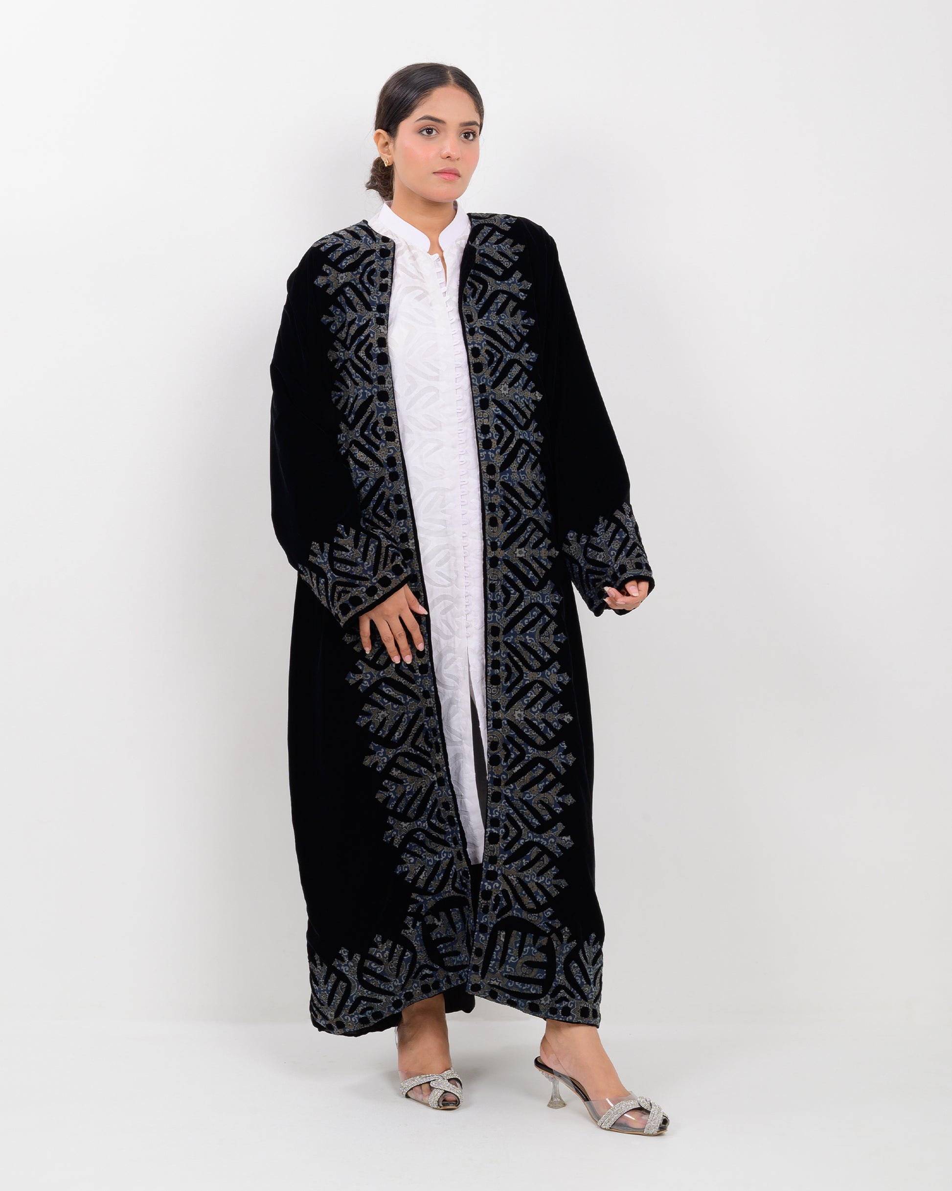 Woman wearing a black applique cutwork velvet long overcoat outfit on a white background