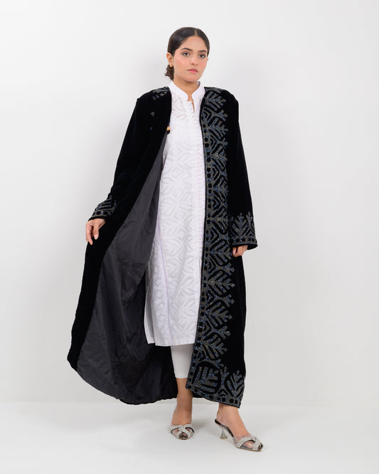 Woman wearing a black applique cutwork velvet long overcoat outfit on a white background