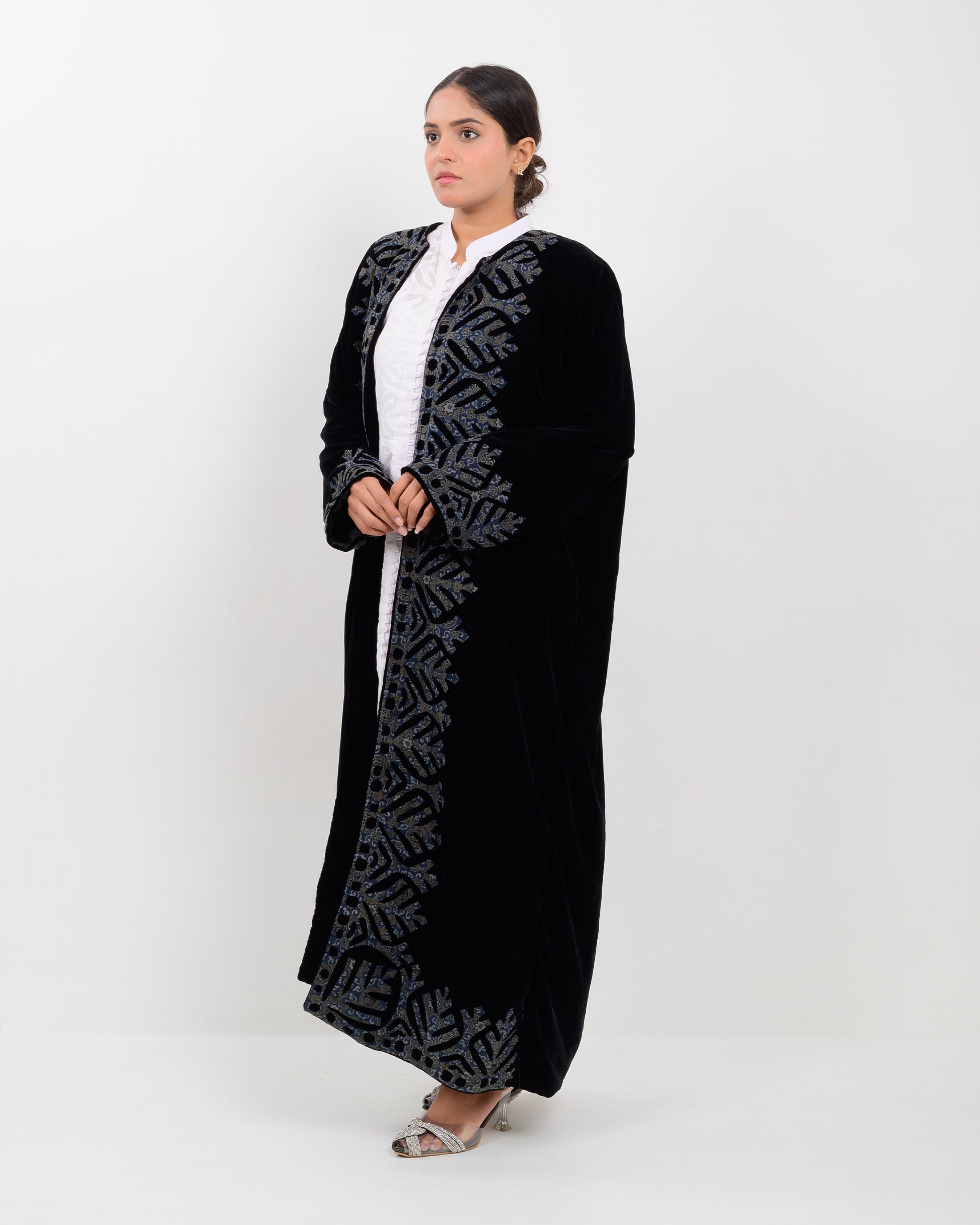 Woman wearing a black applique cutwork velvet long overcoat outfit on a white background