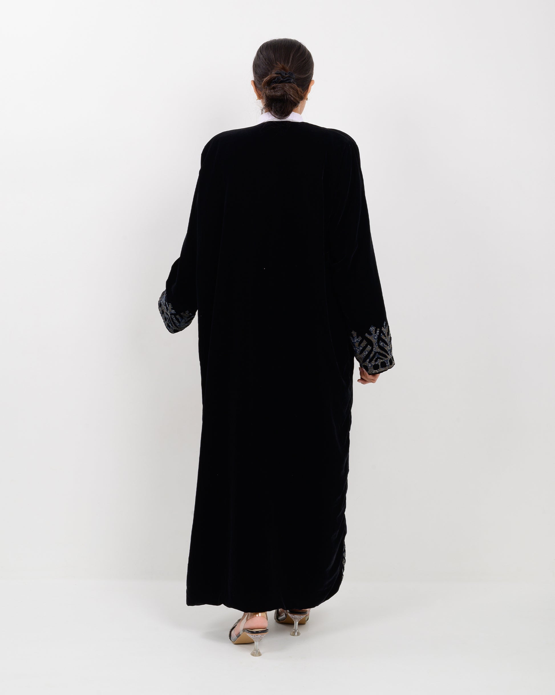 Woman wearing a black applique cutwork velvet long overcoat outfit on a white background