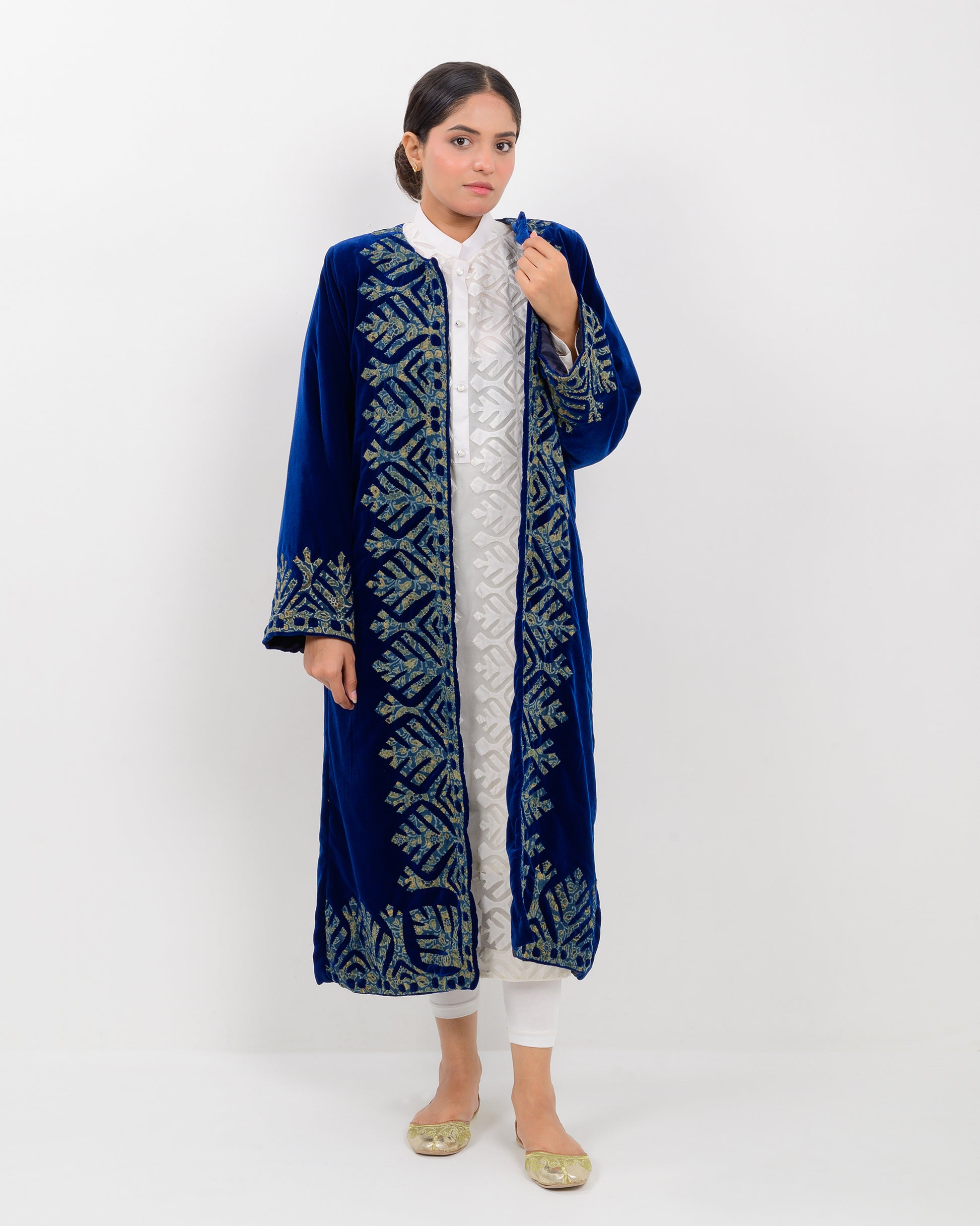 Woman wearing a blue applique cutwork velvet long overcoat outfit on a white background