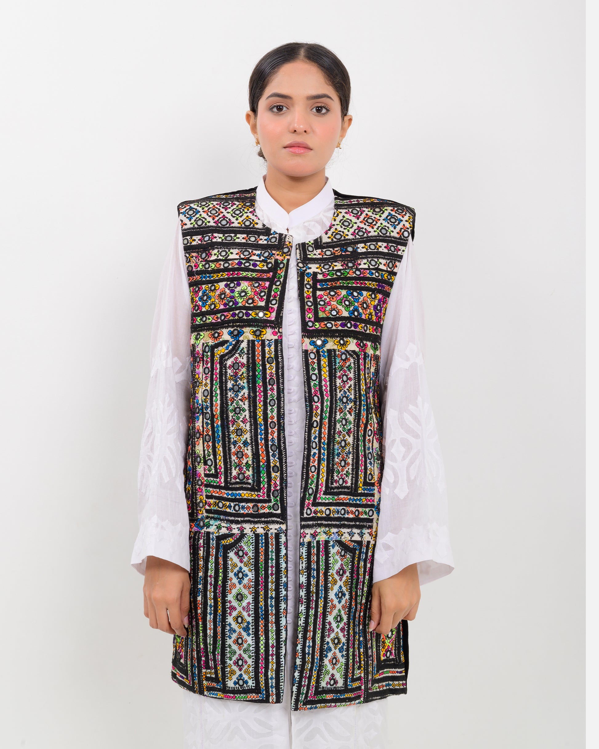 Woman wearing a colorful balochi embroidered vest over a white shirt on a white background