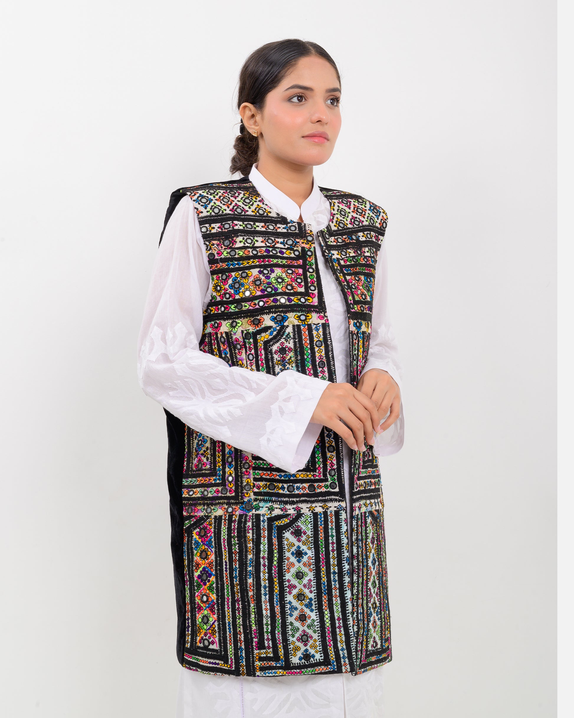 Woman wearing a colorful balochi embroidered vest over a white shirt on a white background
