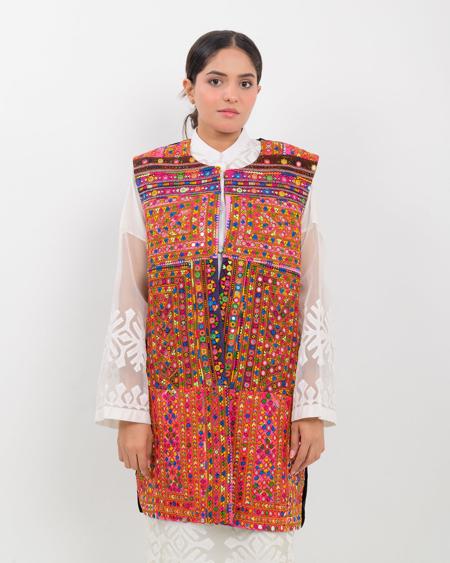 Woman wearing a colorful, patterned Balochi embroidery vest over a white shirt on a white background