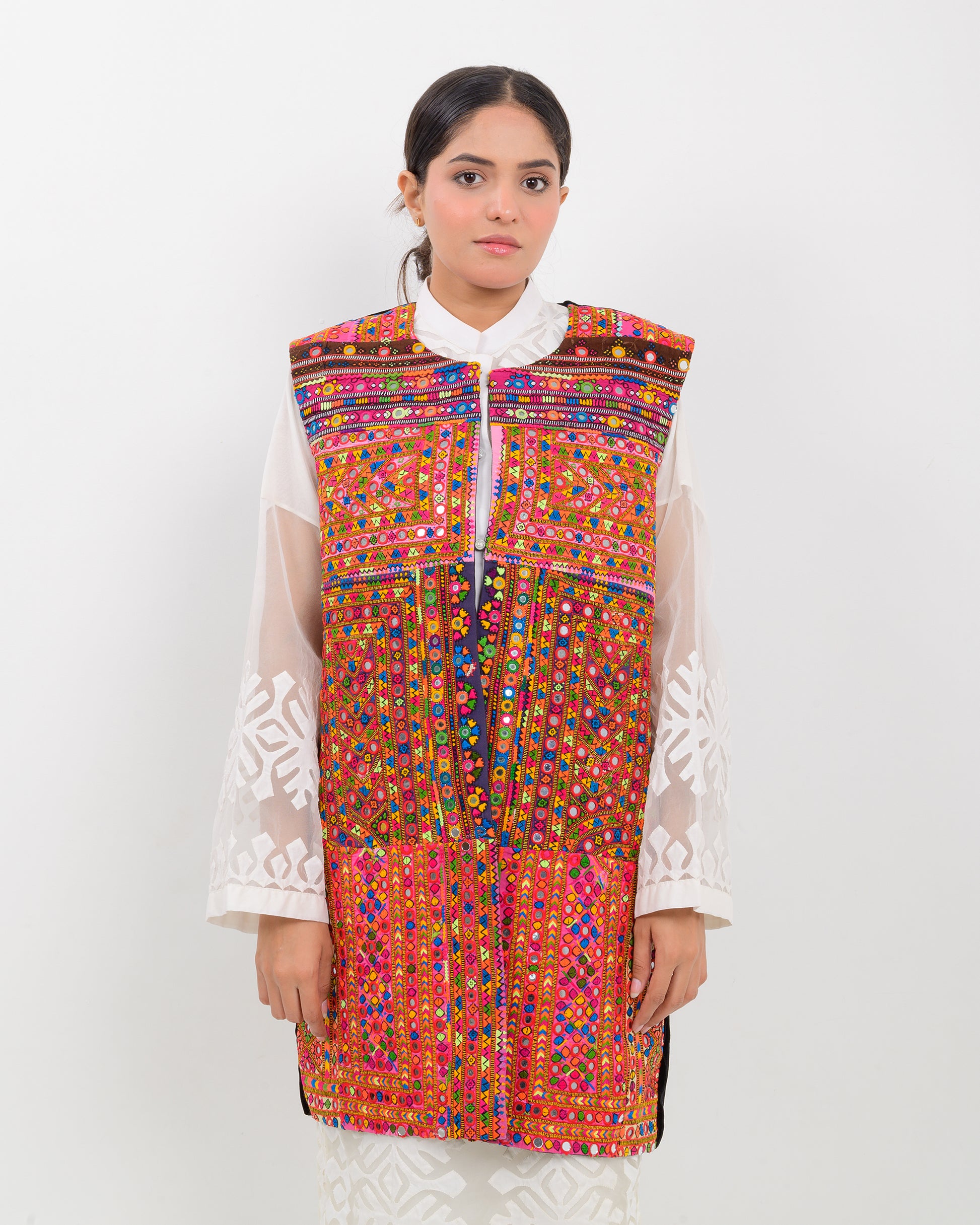 Woman wearing a colorful, patterned Balochi embroidery vest over a white shirt on a white background