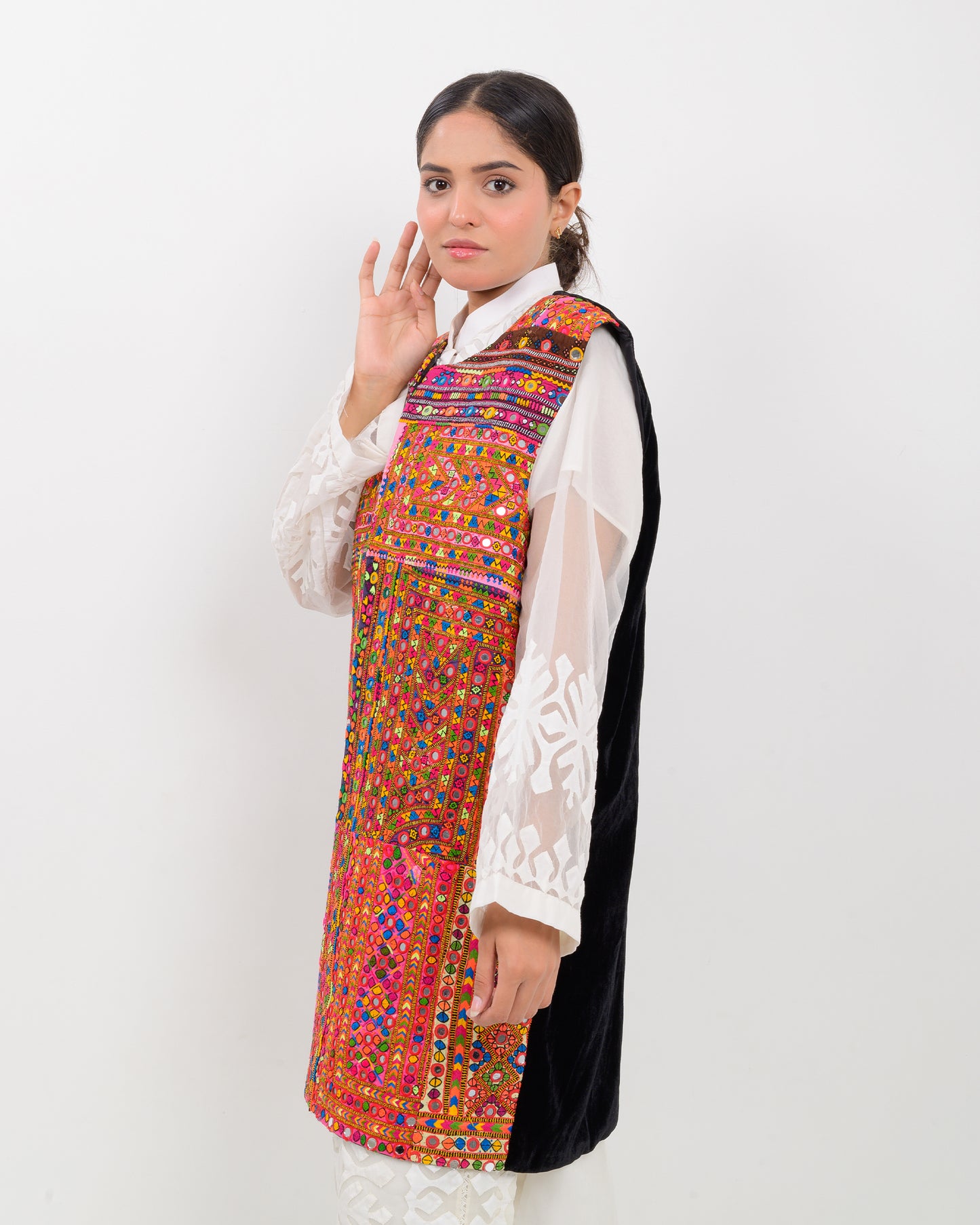Woman wearing a colorful, patterned Balochi embroidery vest over a white shirt on a white background
