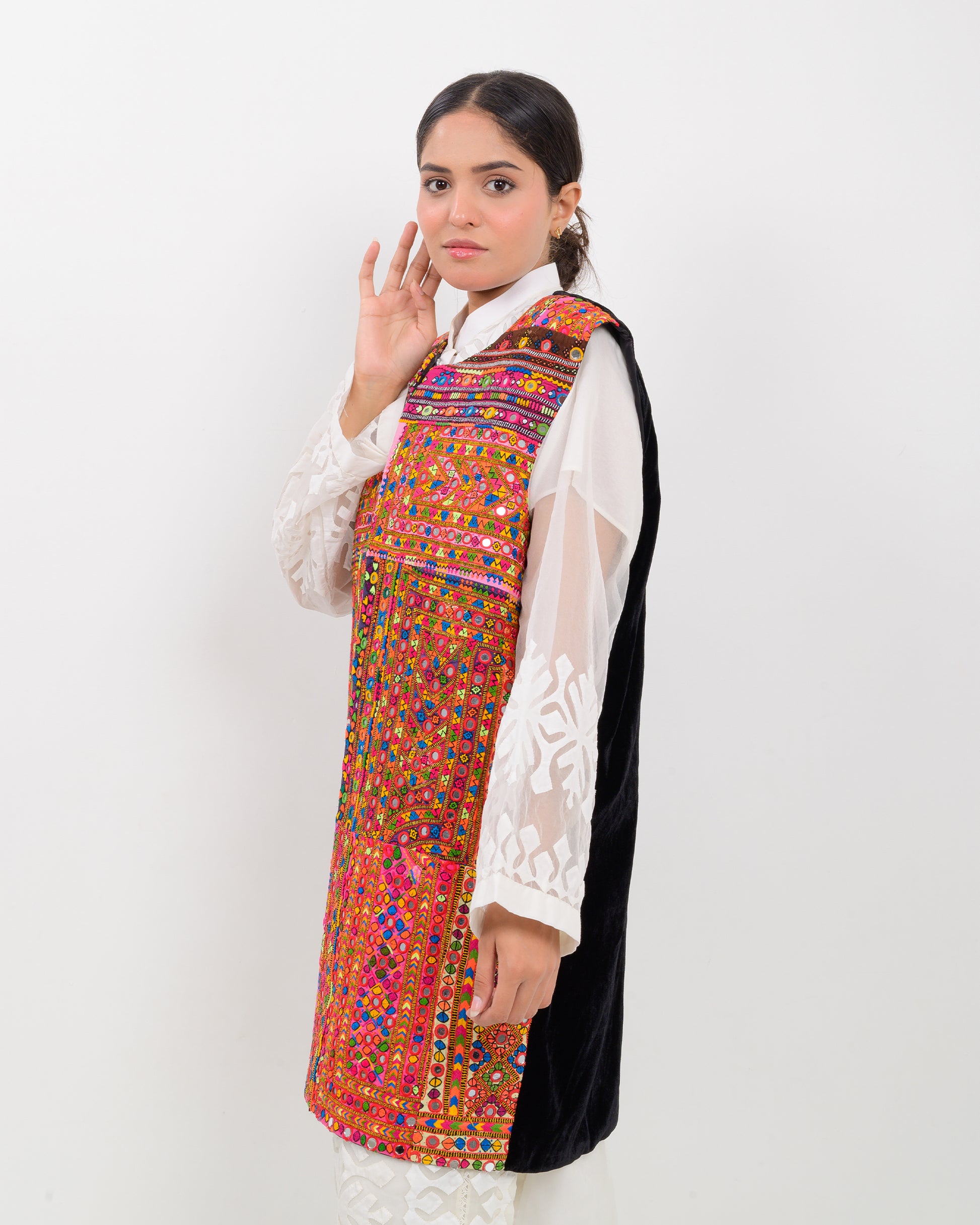 Woman wearing a colorful, patterned Balochi embroidery vest over a white shirt on a white background