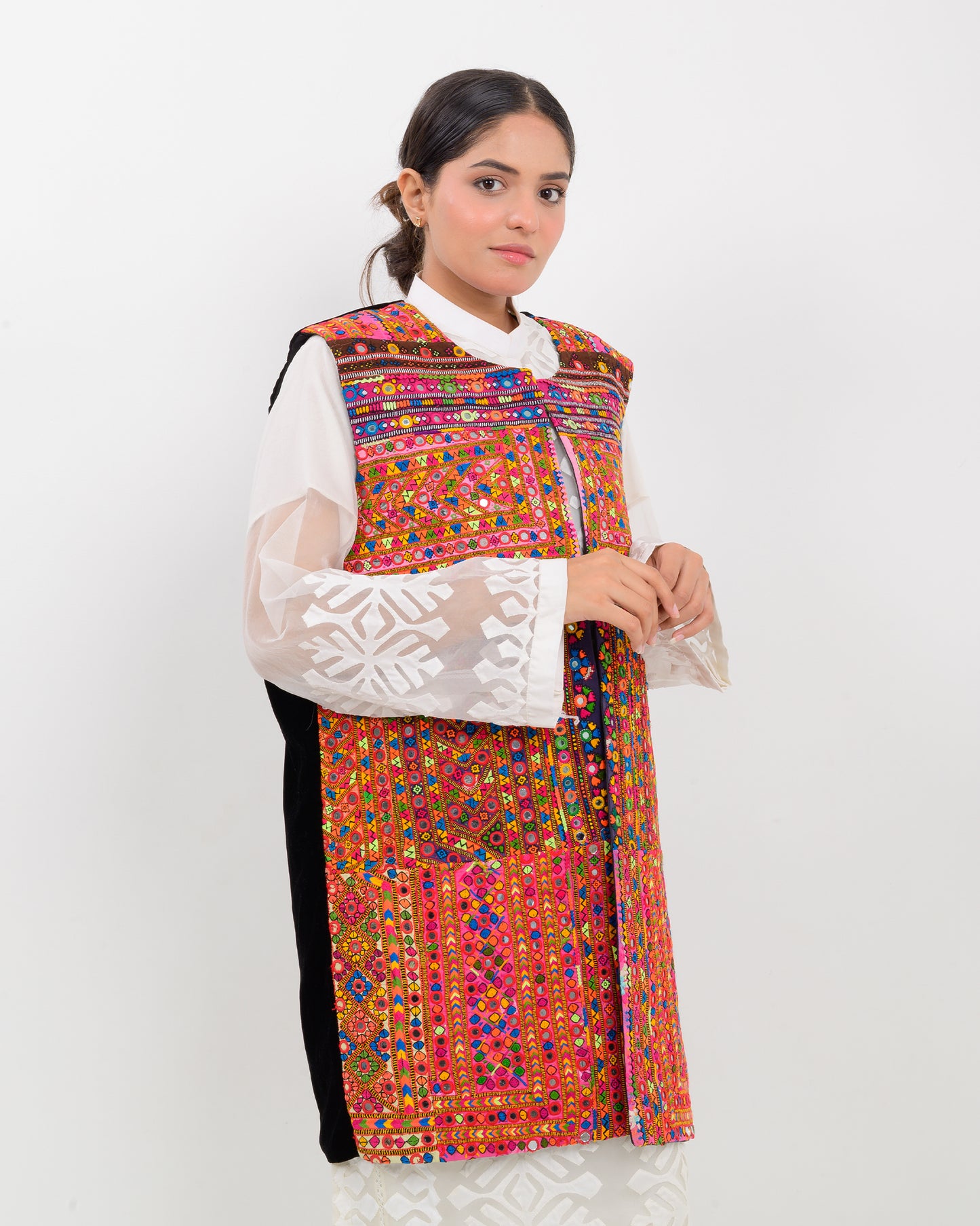 Woman wearing a colorful, patterned Balochi embroidery vest over a white shirt on a white background