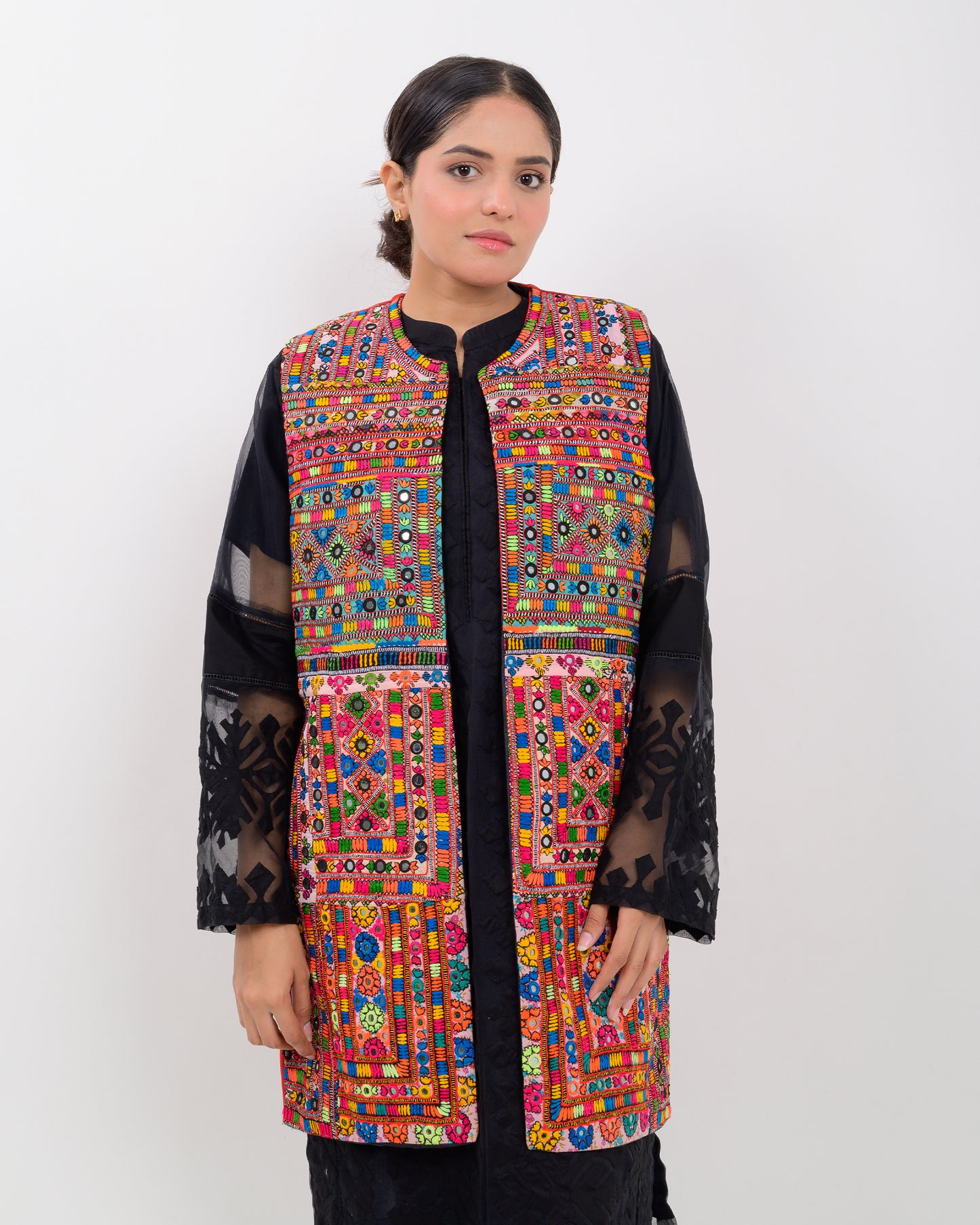 A woman wearing a colorful, patterned Balochi embroidery vest over a black outfit on a white background