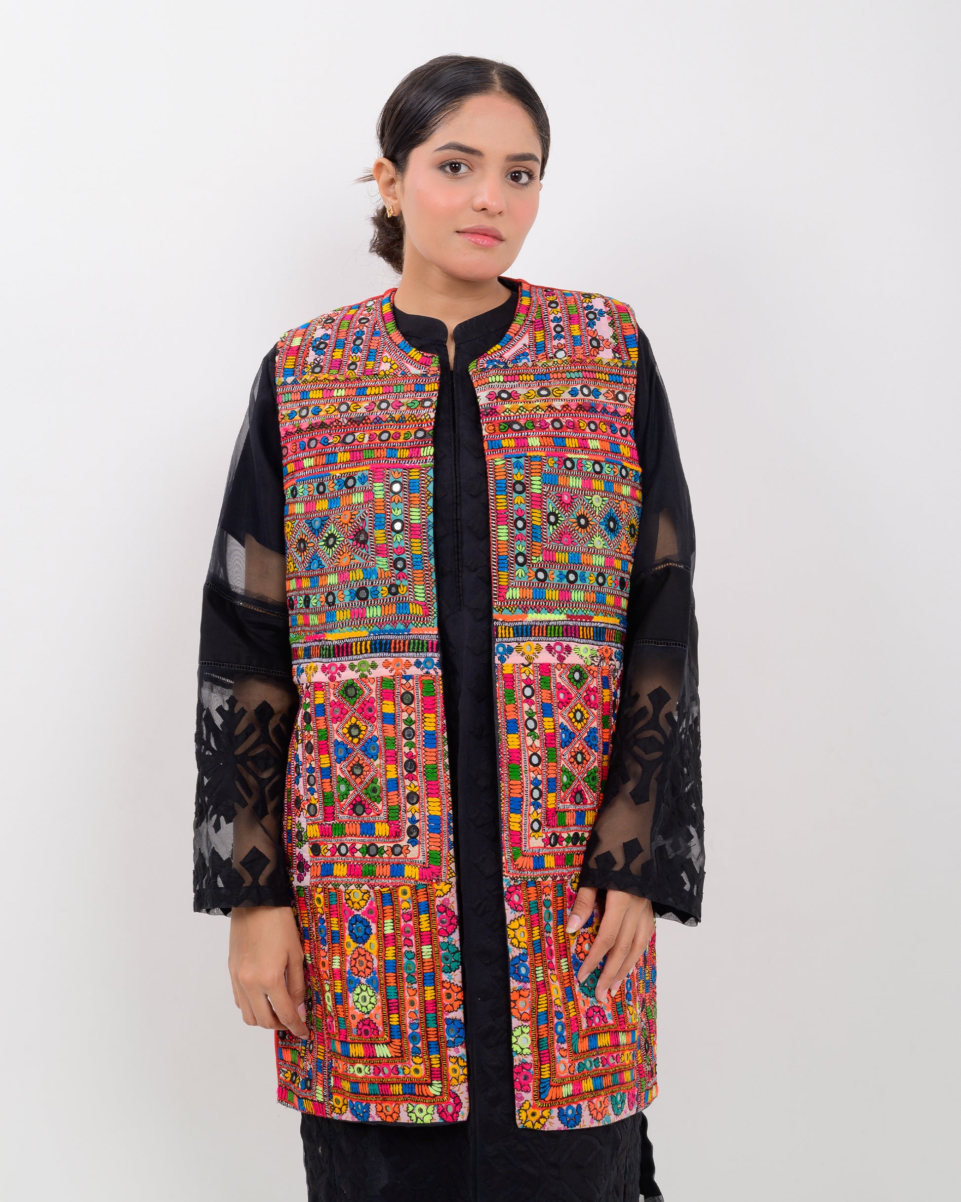 A woman wearing a colorful, patterned Balochi embroidery vest over a black outfit on a white background