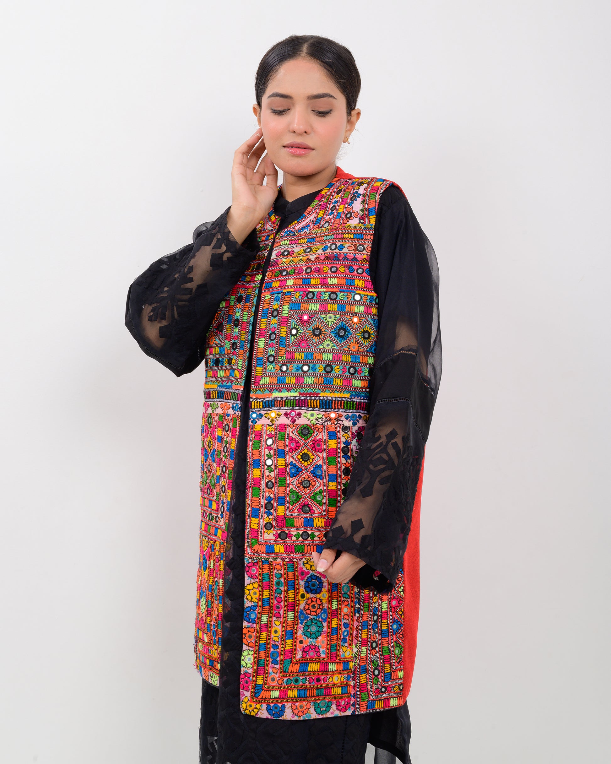 A woman wearing a colorful, patterned Balochi embroidery vest over a black outfit on a white background
