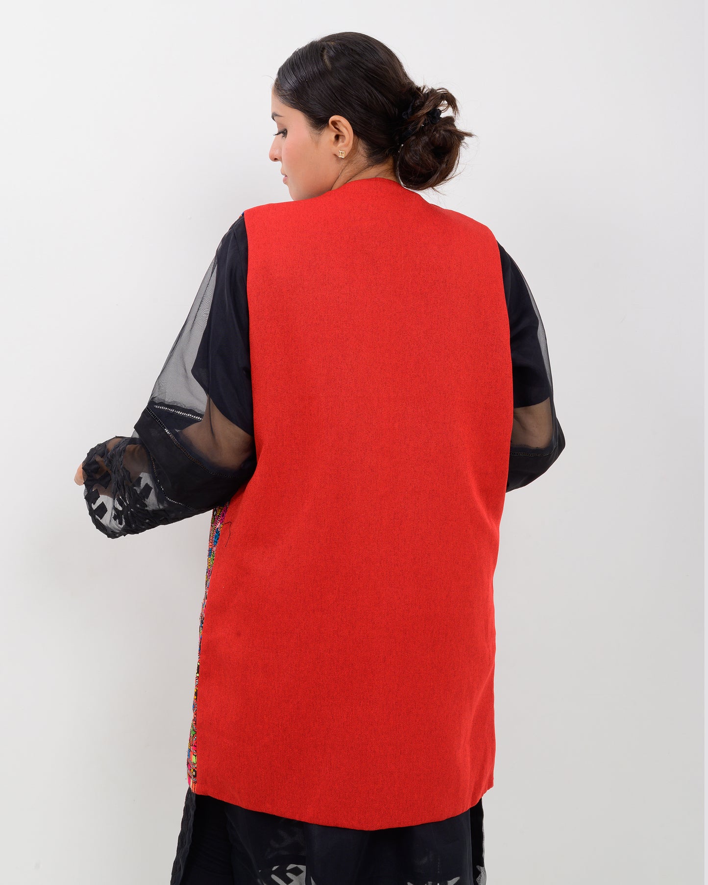 A woman wearing a colorful, patterned Balochi embroidery vest over a black outfit on a white background