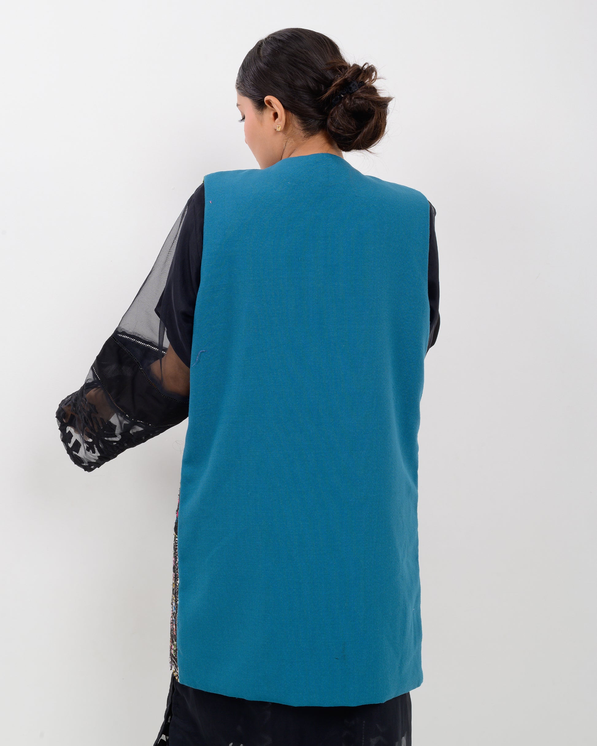 Woman wearing a colorful balochi embroidered vest over a black outfit on a white background