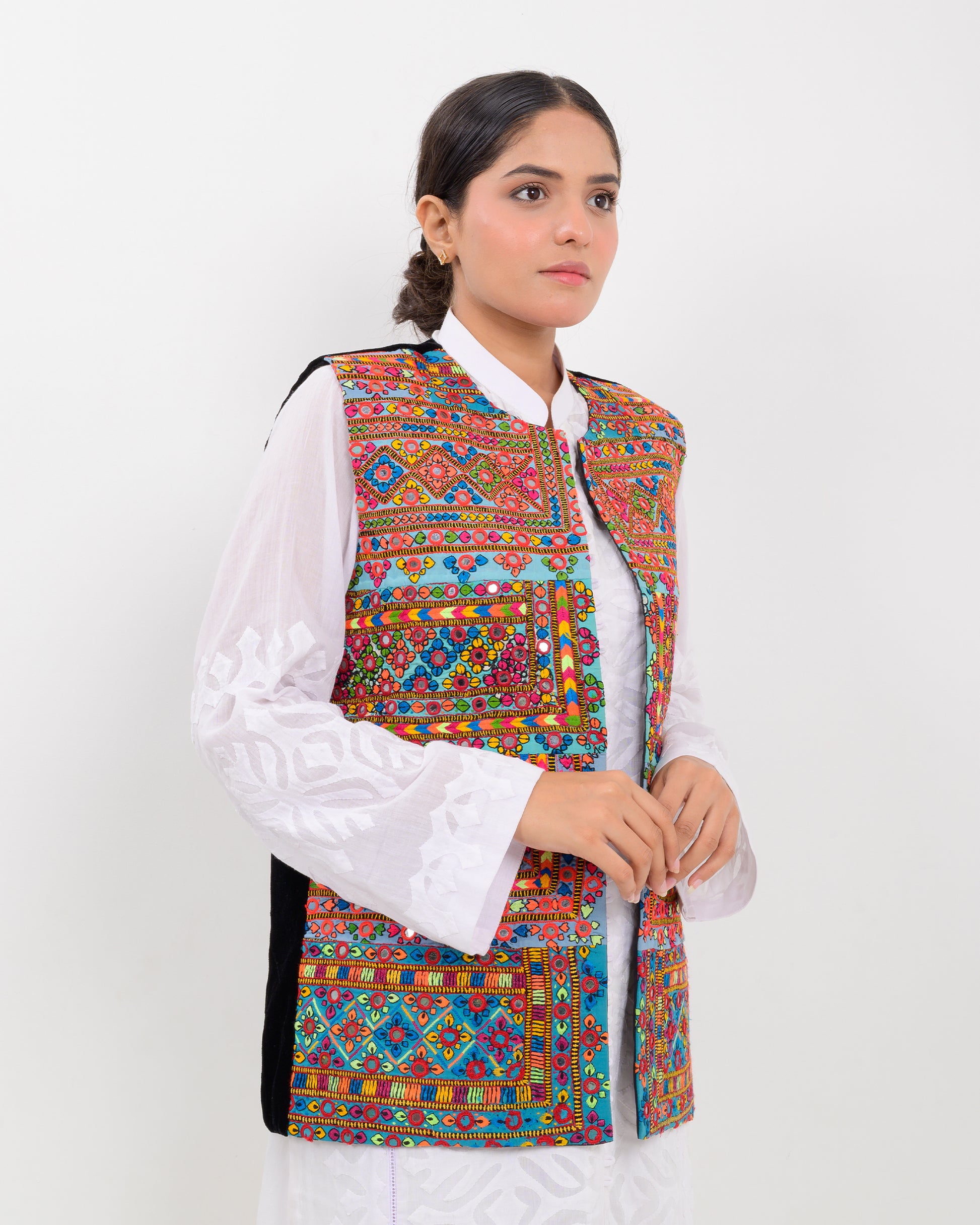 Woman wearing a colorful patterned Balochi embroidery vest over a white shirt on a white background