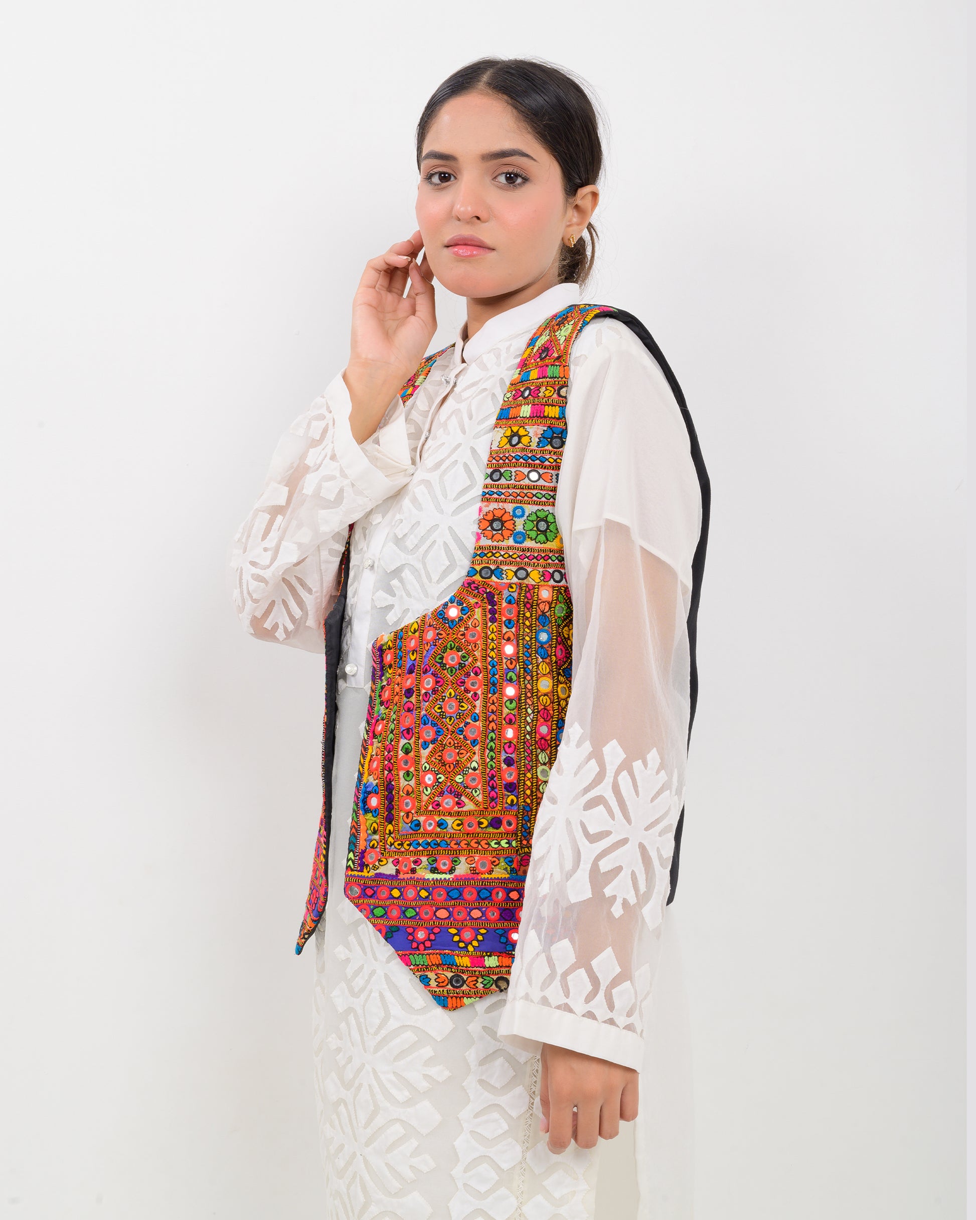 Woman wearing a colorful patterned Balochi embroidery vest over a white outfit on a white background