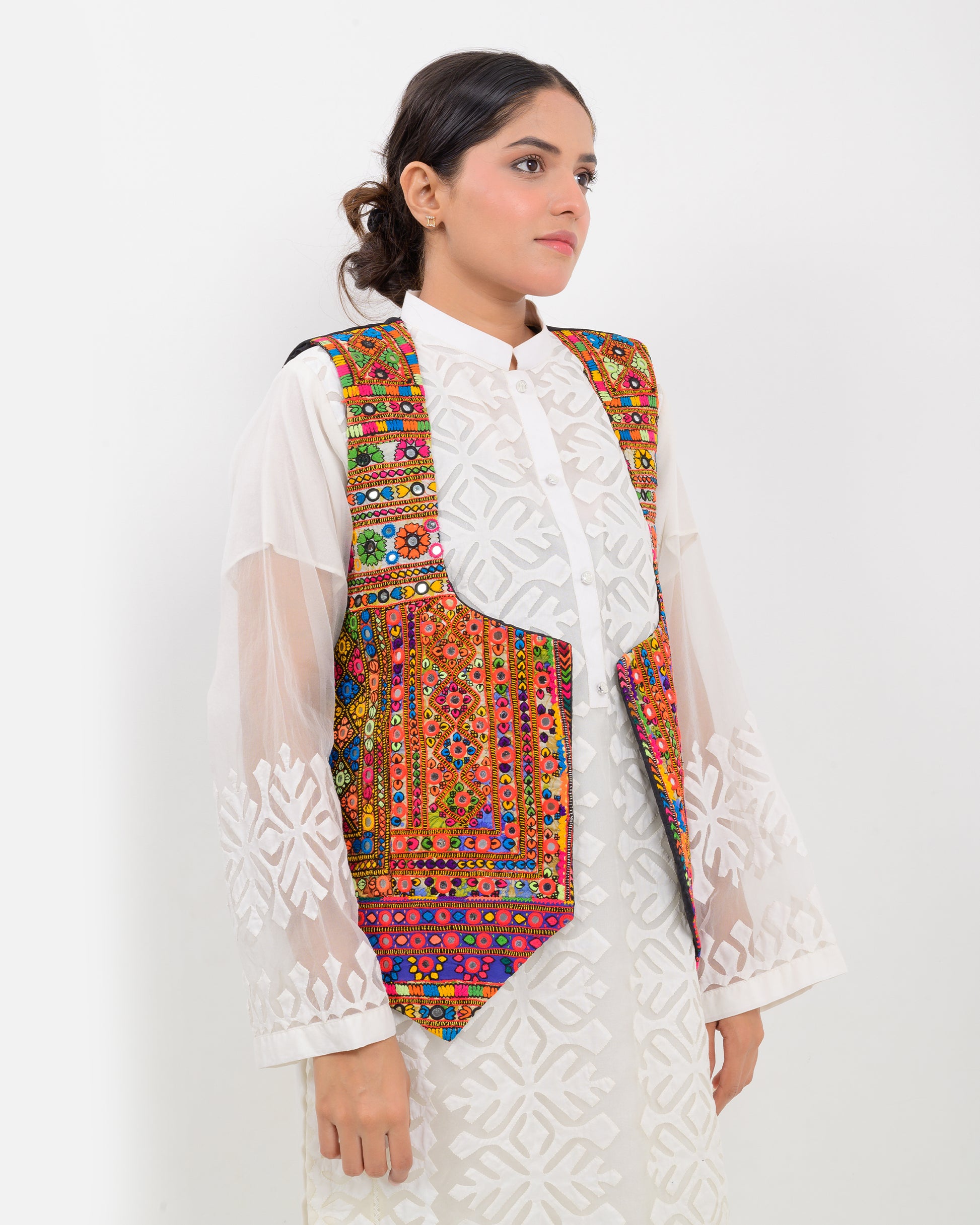 Woman wearing a colorful patterned Balochi embroidery vest over a white outfit on a white background