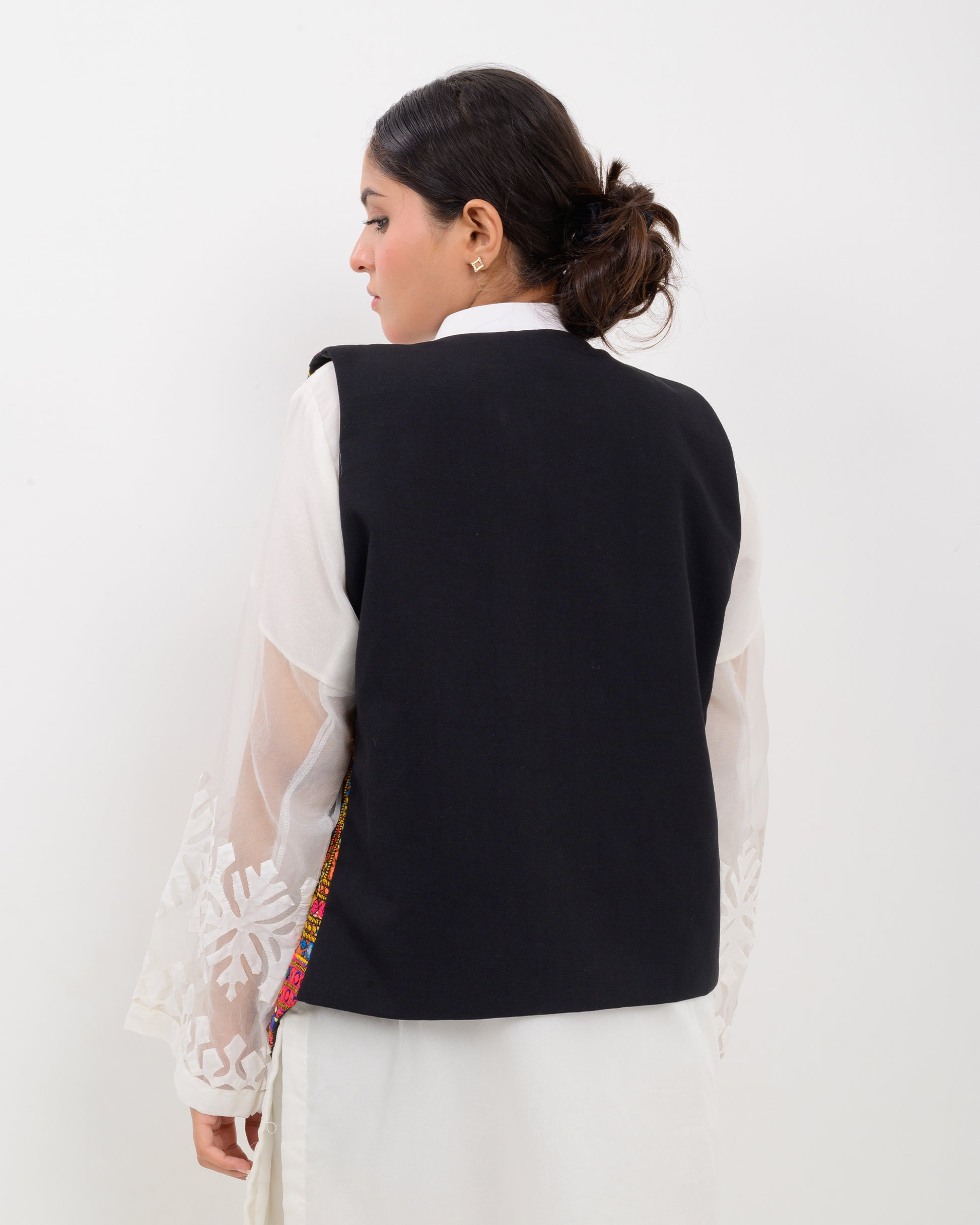 Woman wearing a colorful patterned Balochi embroidery vest over a white outfit on a white background