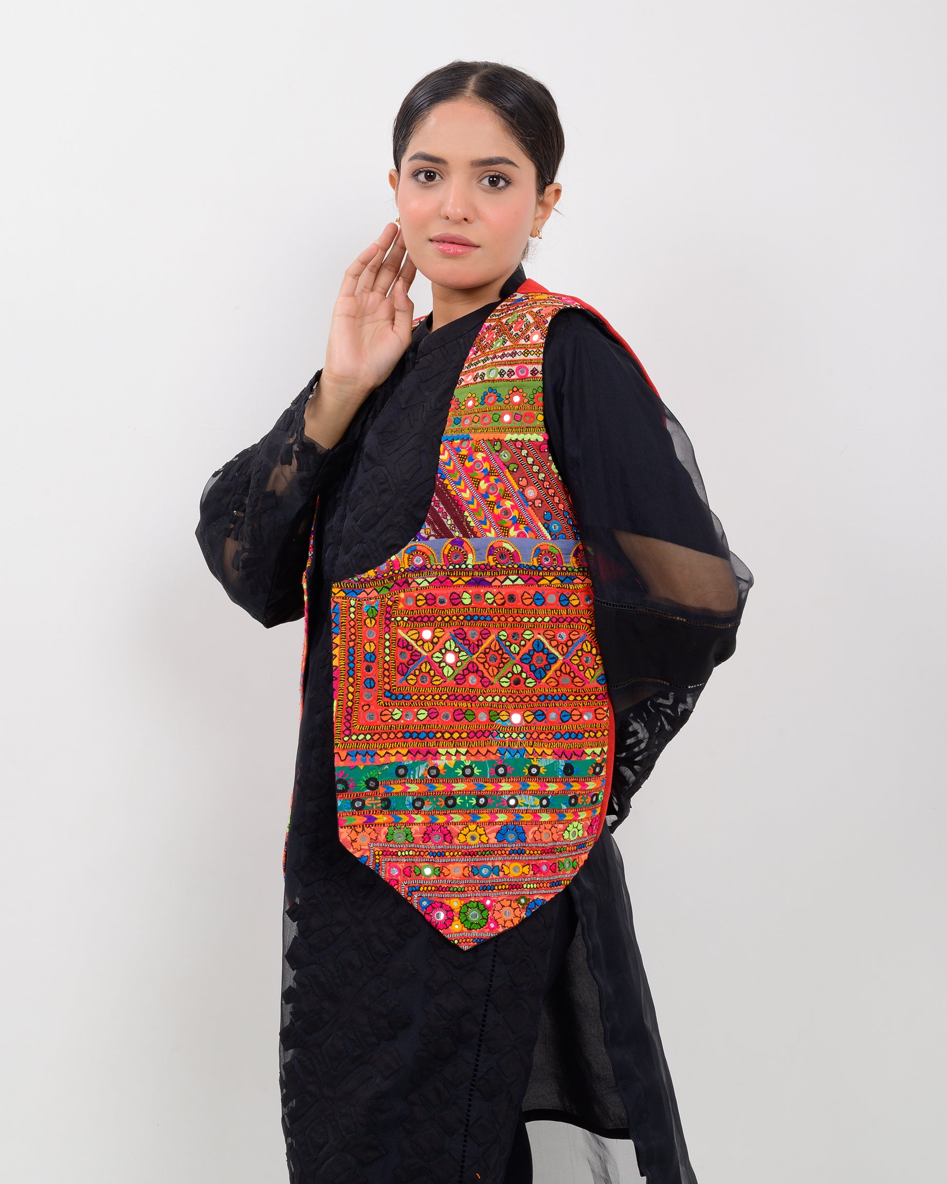 Woman wearing a colorful embroidered vest over a black outfit on a white background