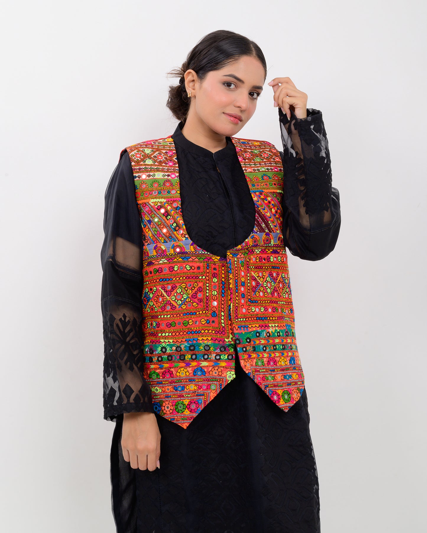 Woman wearing a colorful embroidered vest over a black outfit on a white background