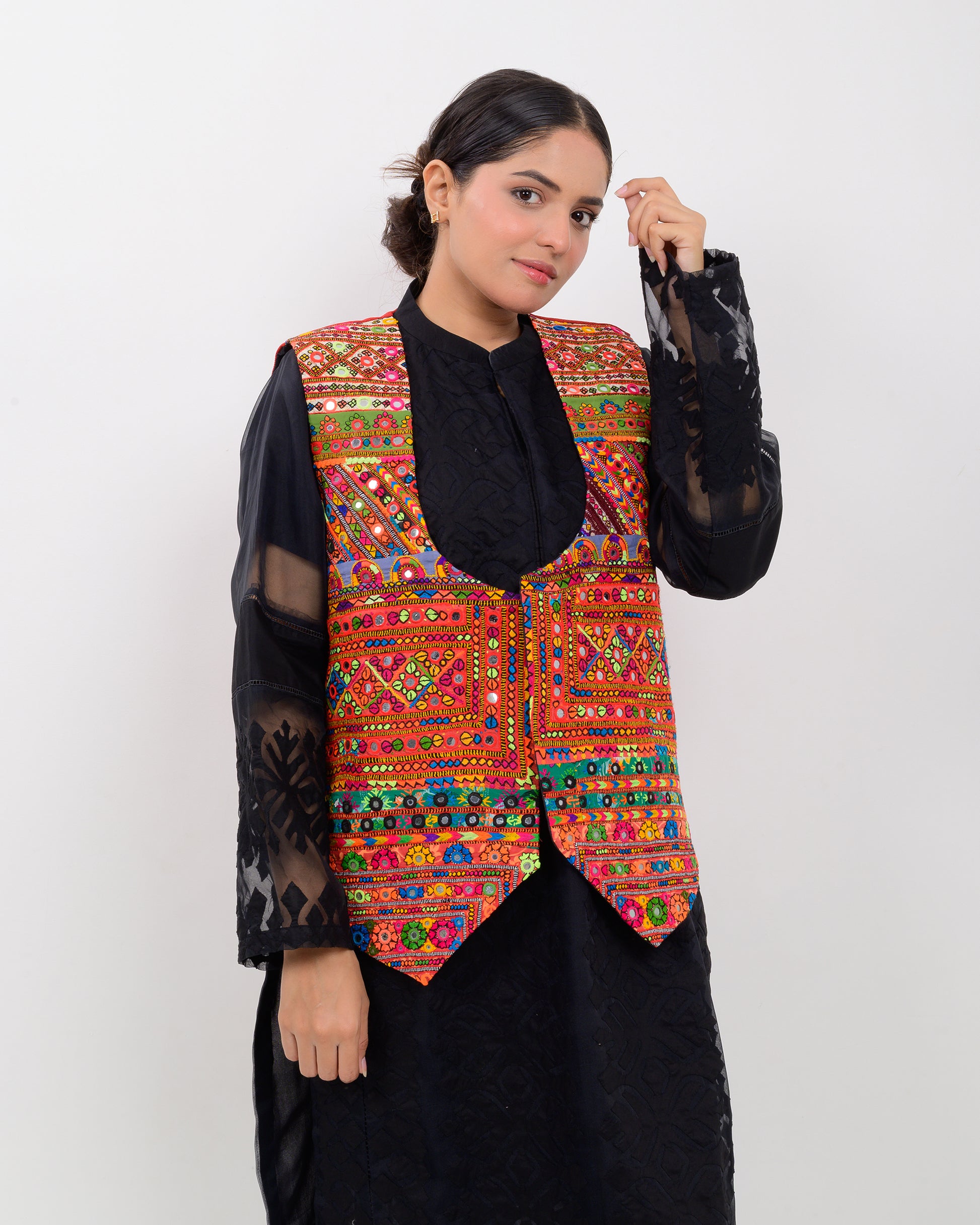 Woman wearing a colorful embroidered vest over a black outfit on a white background