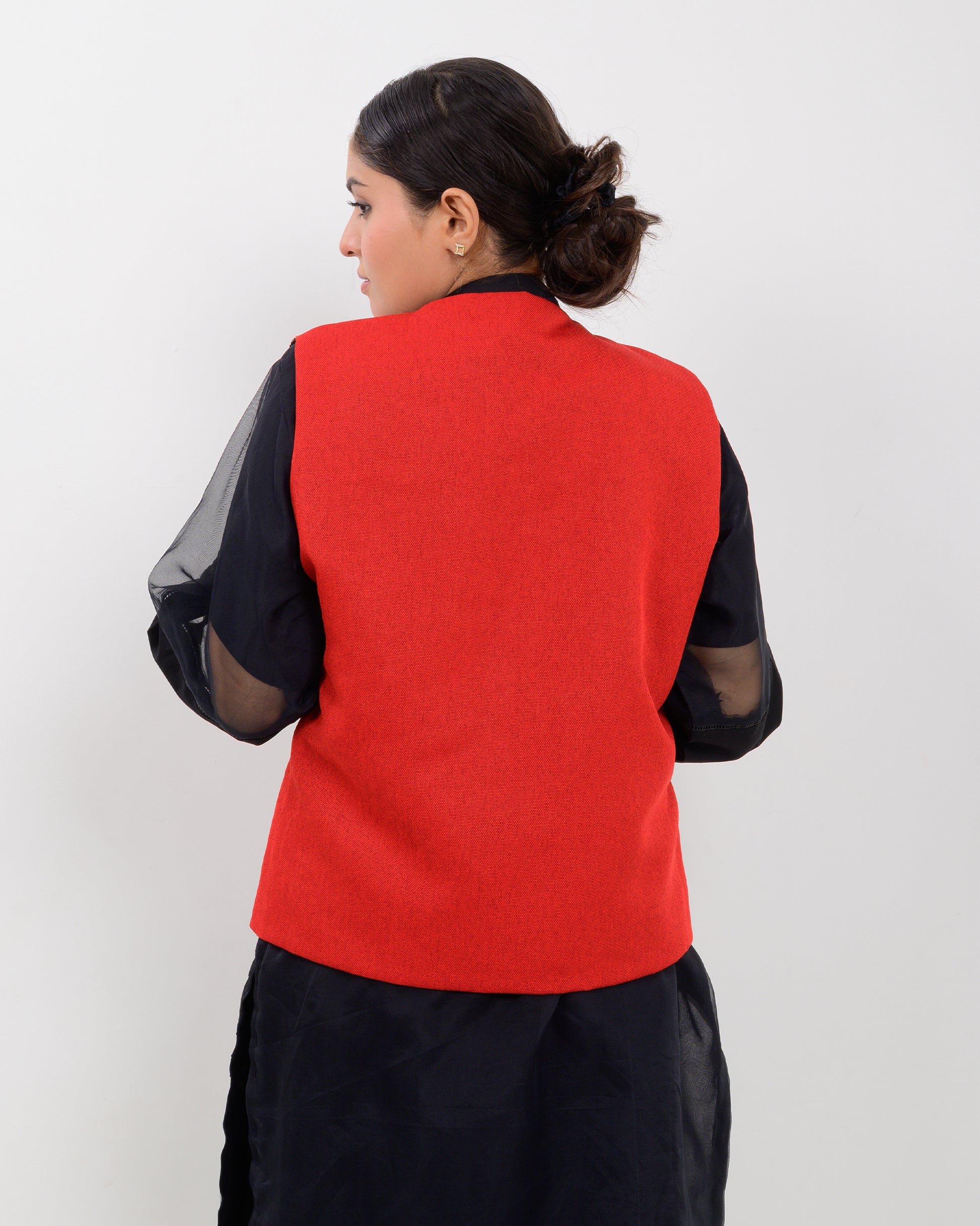 Woman wearing a colorful embroidered vest over a black outfit on a white background